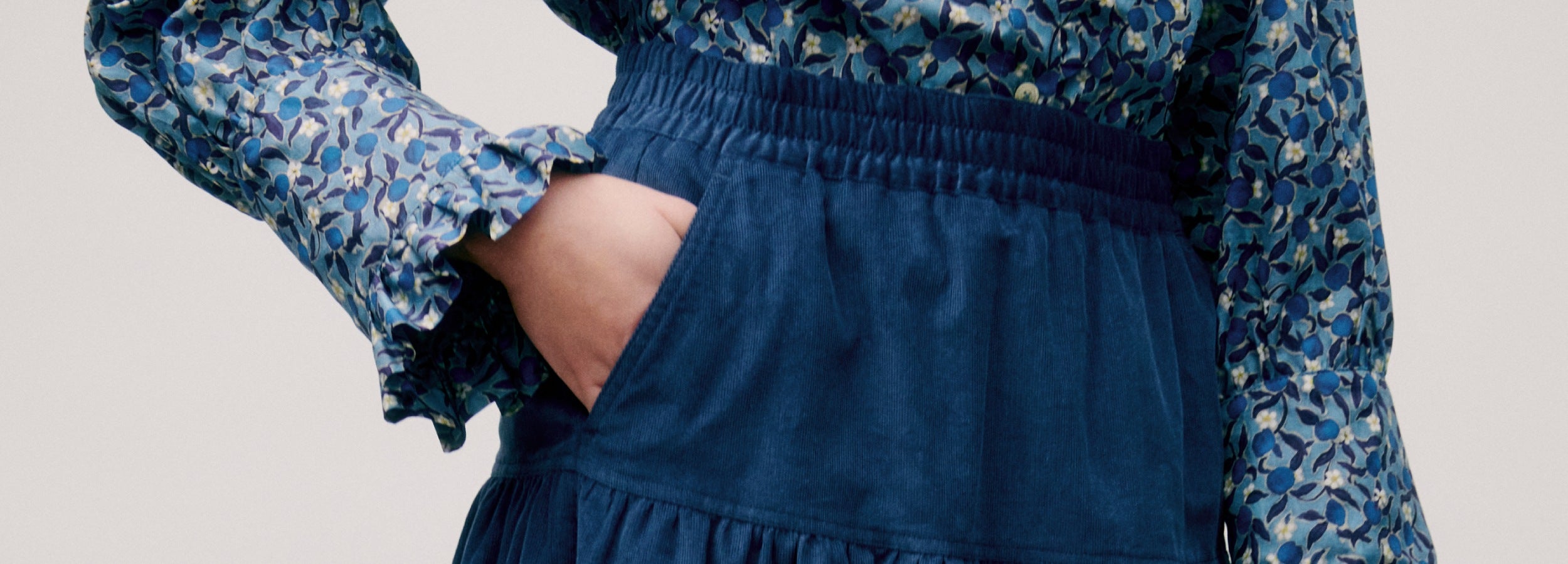 Woman wearing a blue floral blouse with long sleeves and a matching blue corduroy skirt