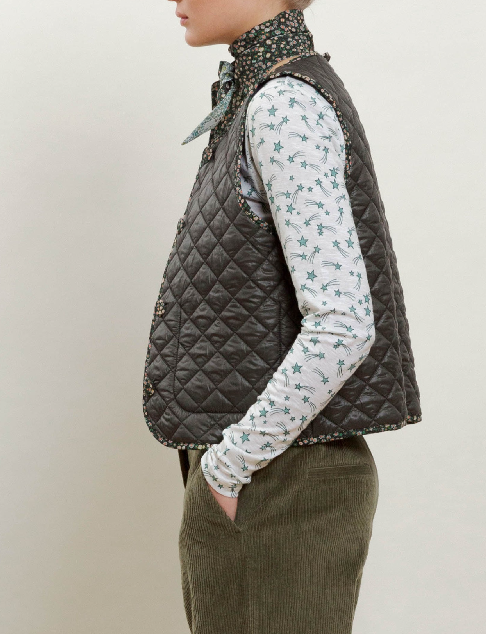 Woman in long-sleeved comet print t-shirt, green quilt vest with buttons and pockets and green corduroy pants