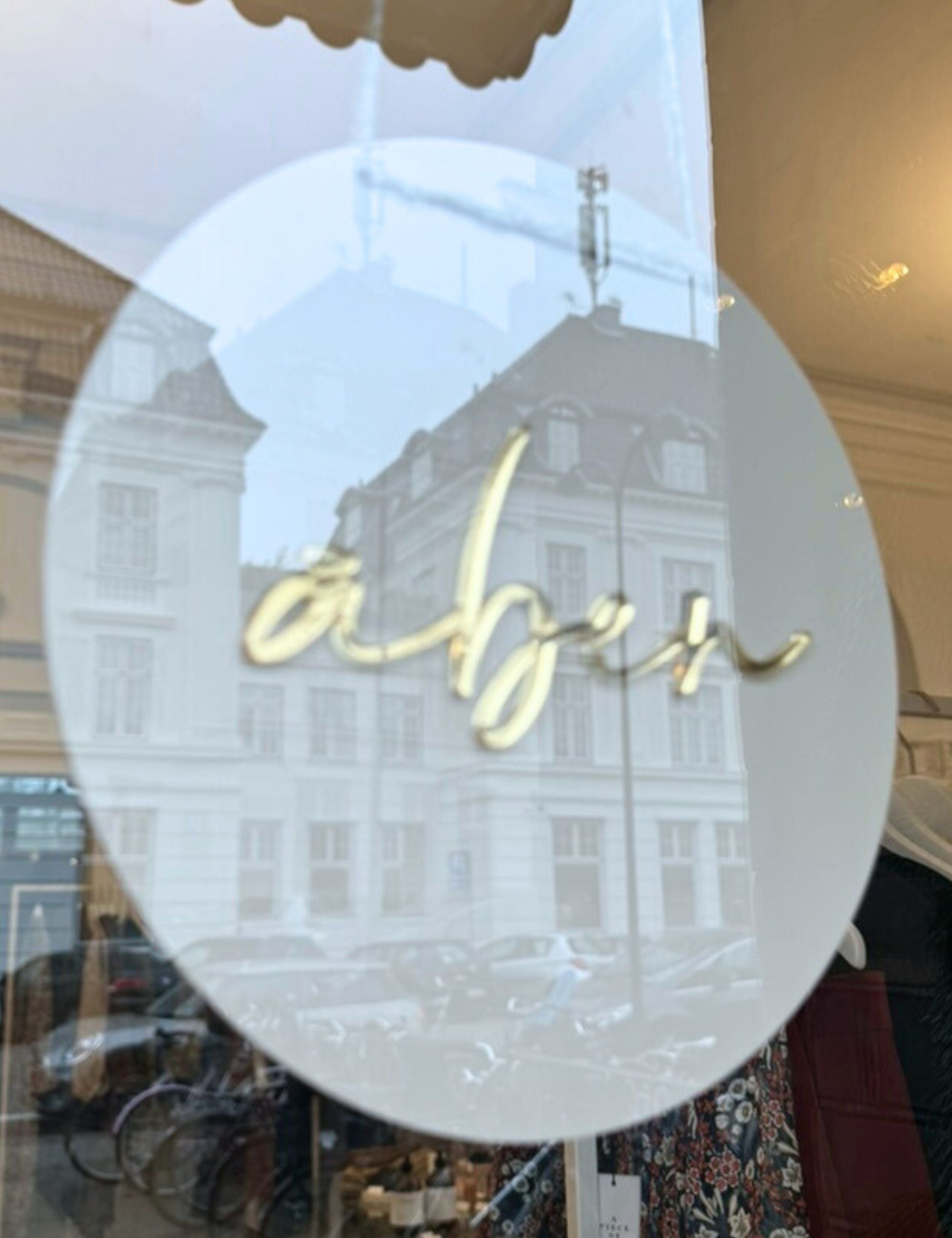 Åben sign on glass door to APOF studio and shop with white houses reflected in the glass