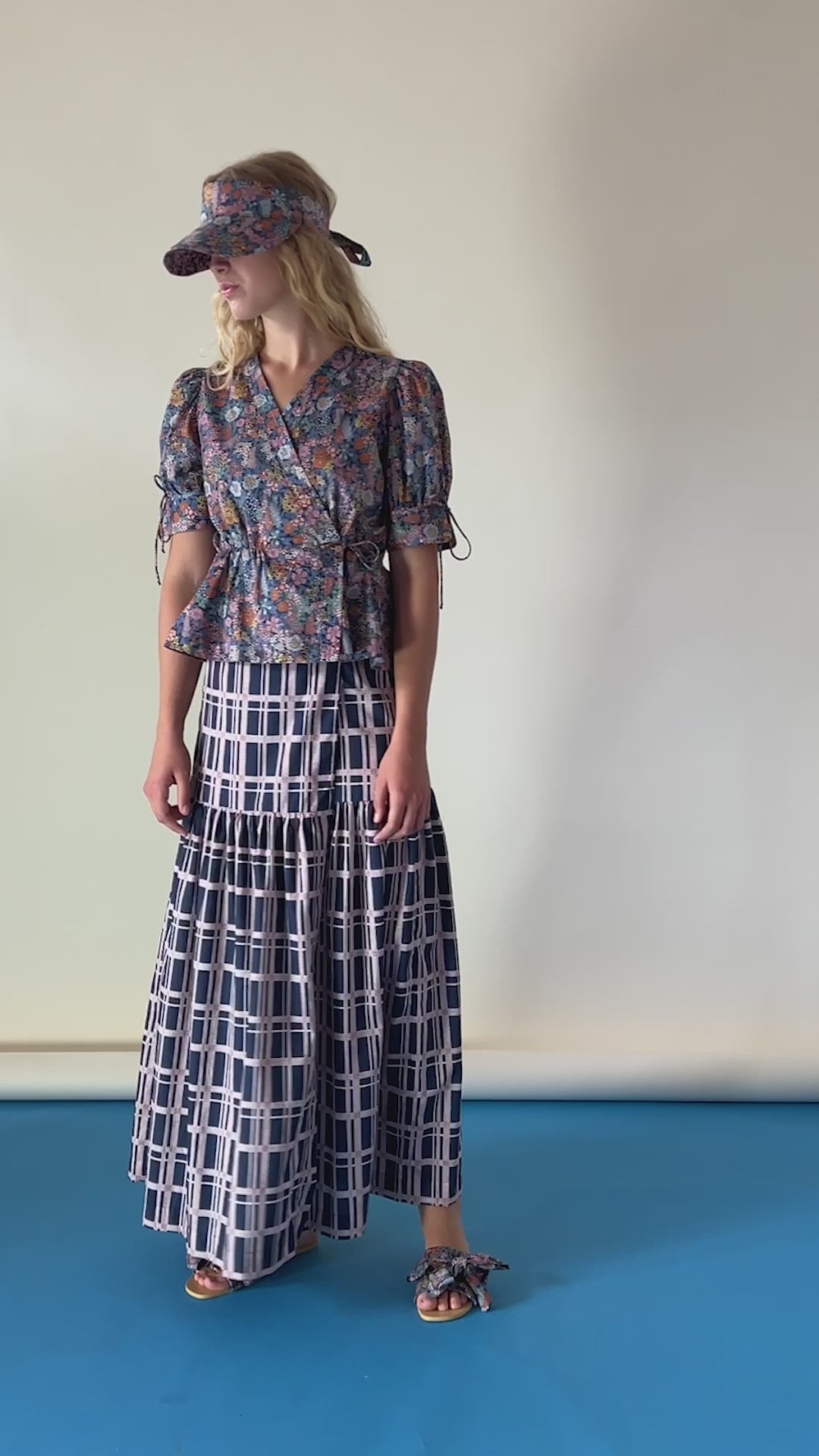 Woman in short sleeved wrap blouse and sun cap with flower pattern and checked maxi skirt