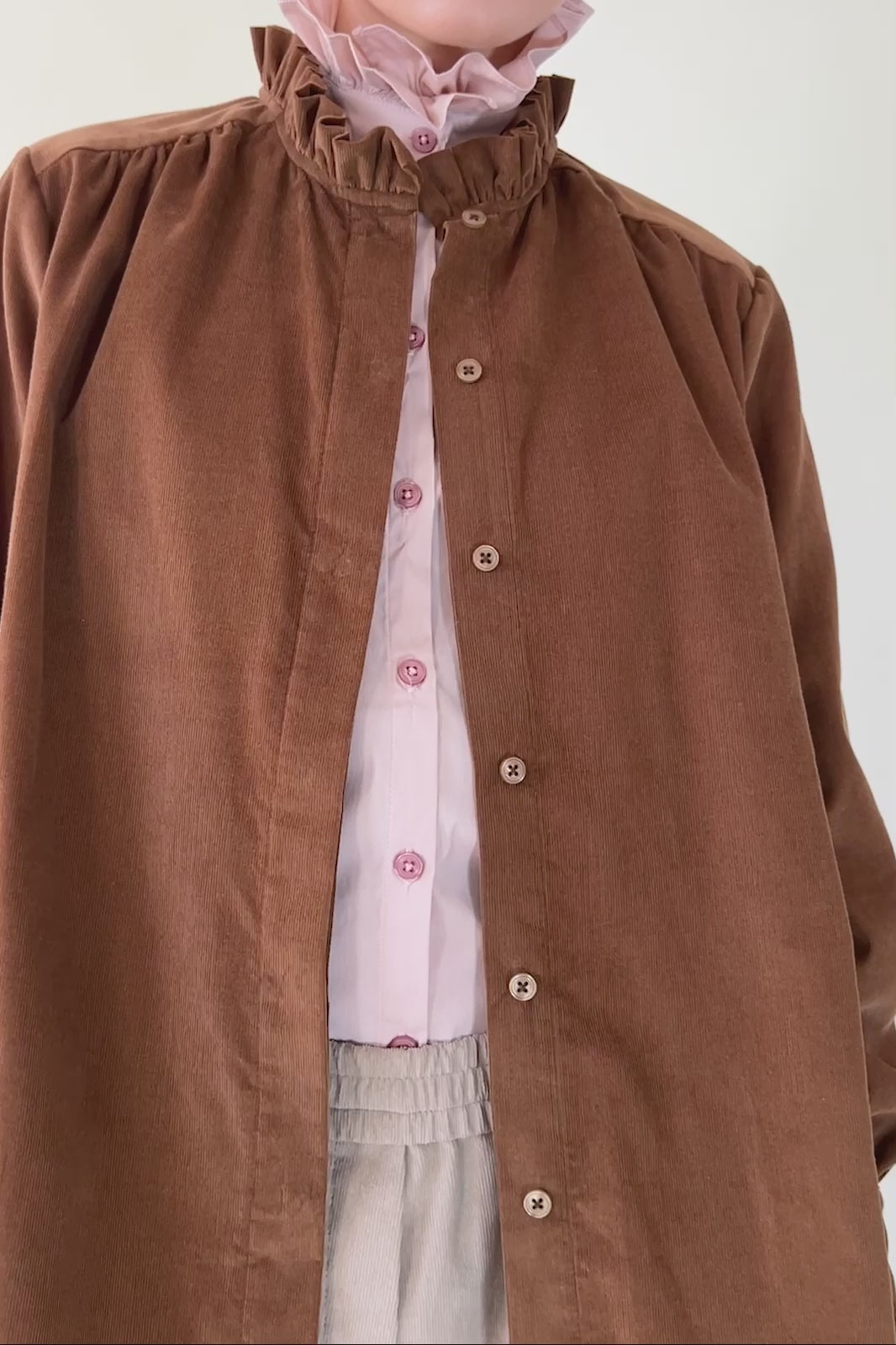 Woman in pink shirt with frilled stand collar and cognac brown baby corduroy jacket with frill collar