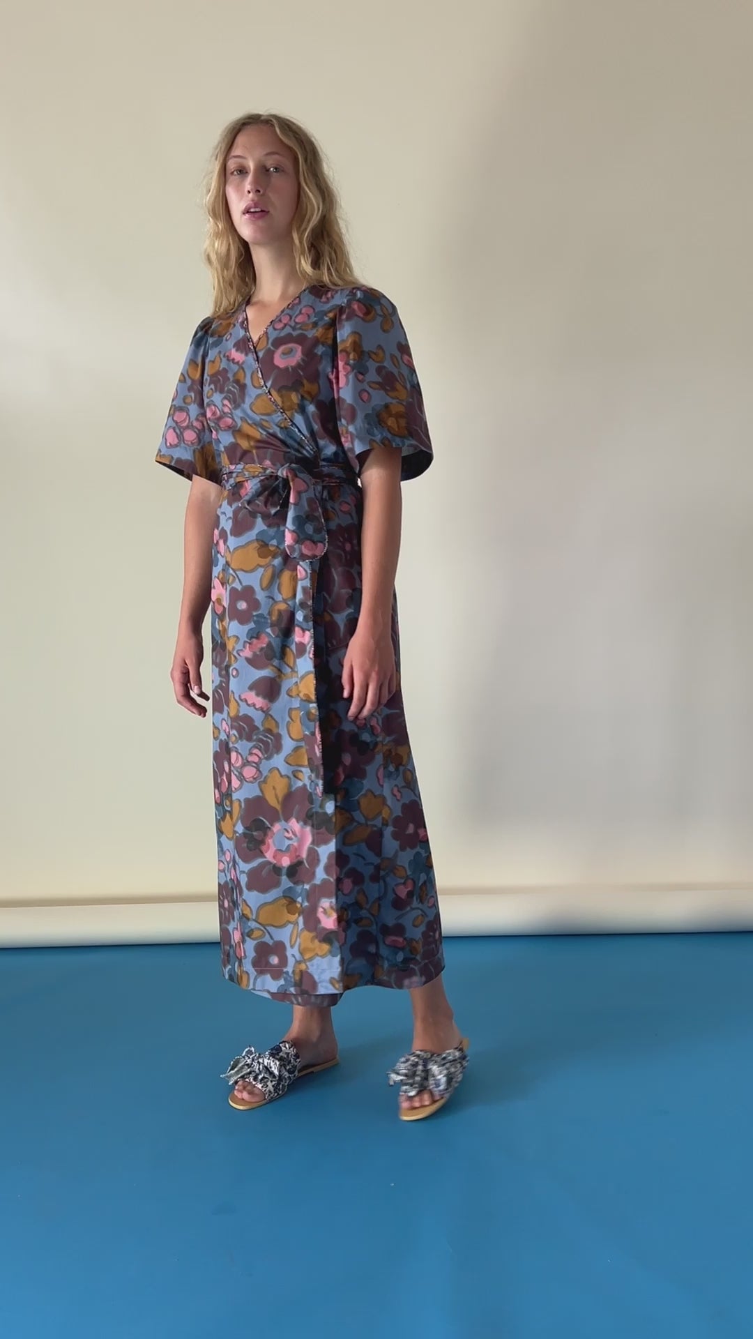 Woman in blue pink and burgundy flower patterned wrap dress in Liberty cotton with short sleeves and sandals with bows