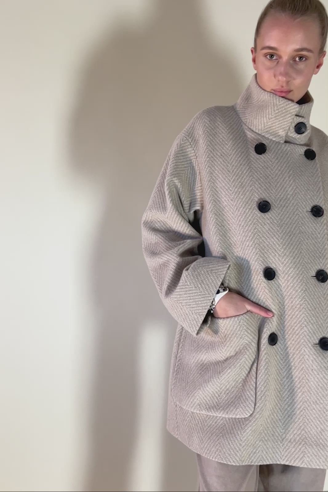 Woman in beige herringbone patterned jacket with large pockets black buttons and belt