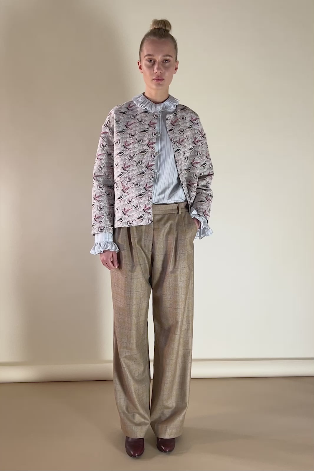 Woman in wide beige check print wool pants, blue and white striped hirt with frills and jacquard jacket with sparrow print