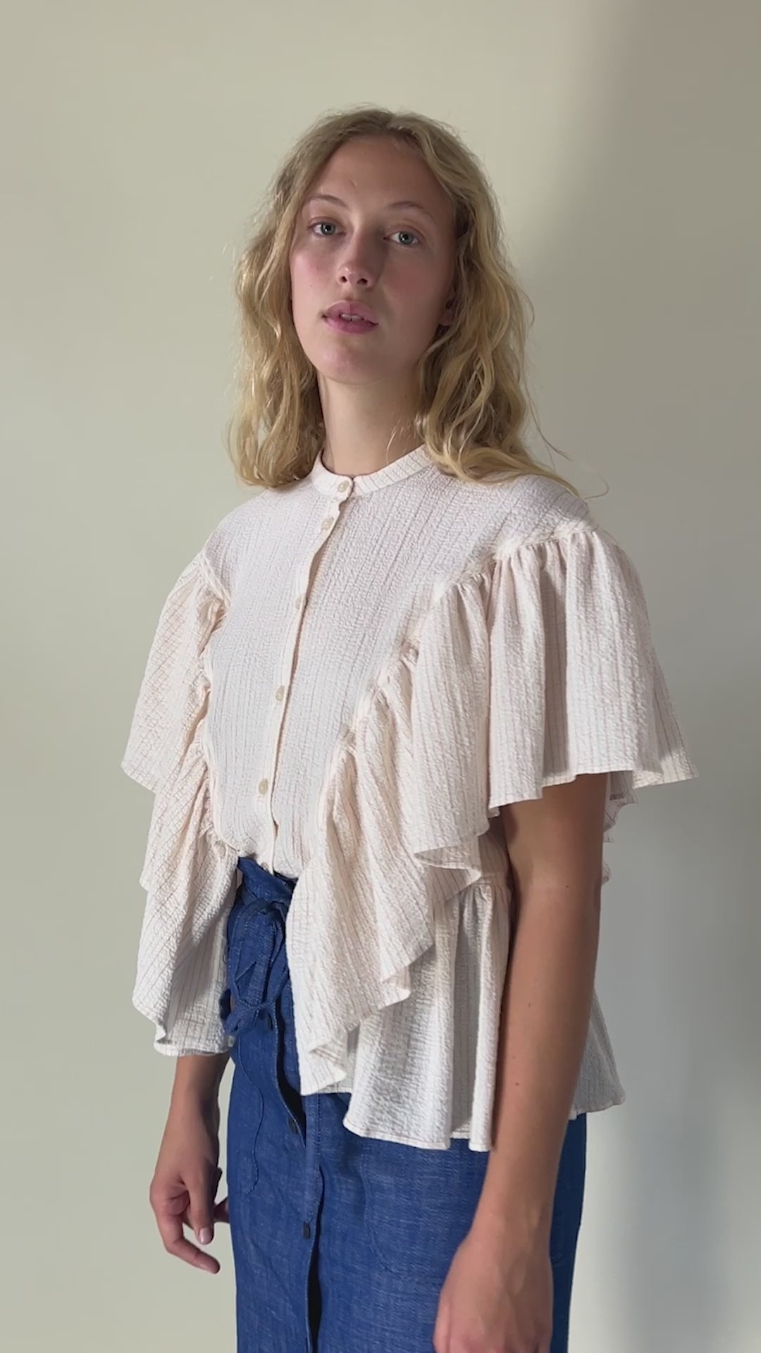 Woman in pink short sleeved blouse with stripes and frills and blue skirt