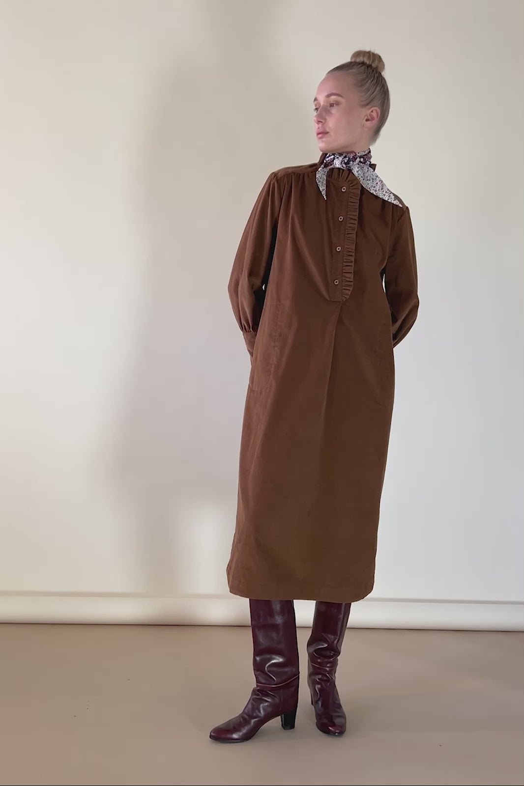 Woman in cognac colored baby corduroy dress with floral print bandana around neck and brown boots