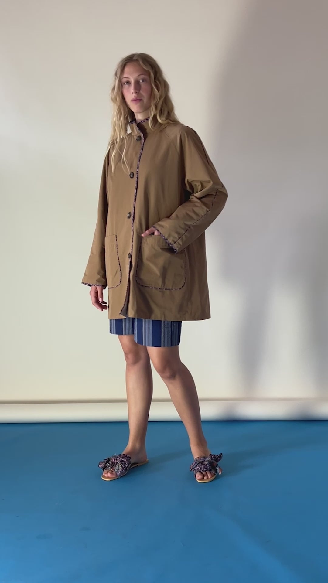 Blonde woman in brown jacket, blue striped shorts and sandals with bows