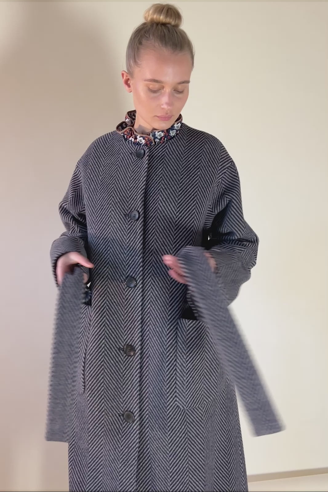 Woman in blue herringbone patterned coat with large pockets black buttons and belt