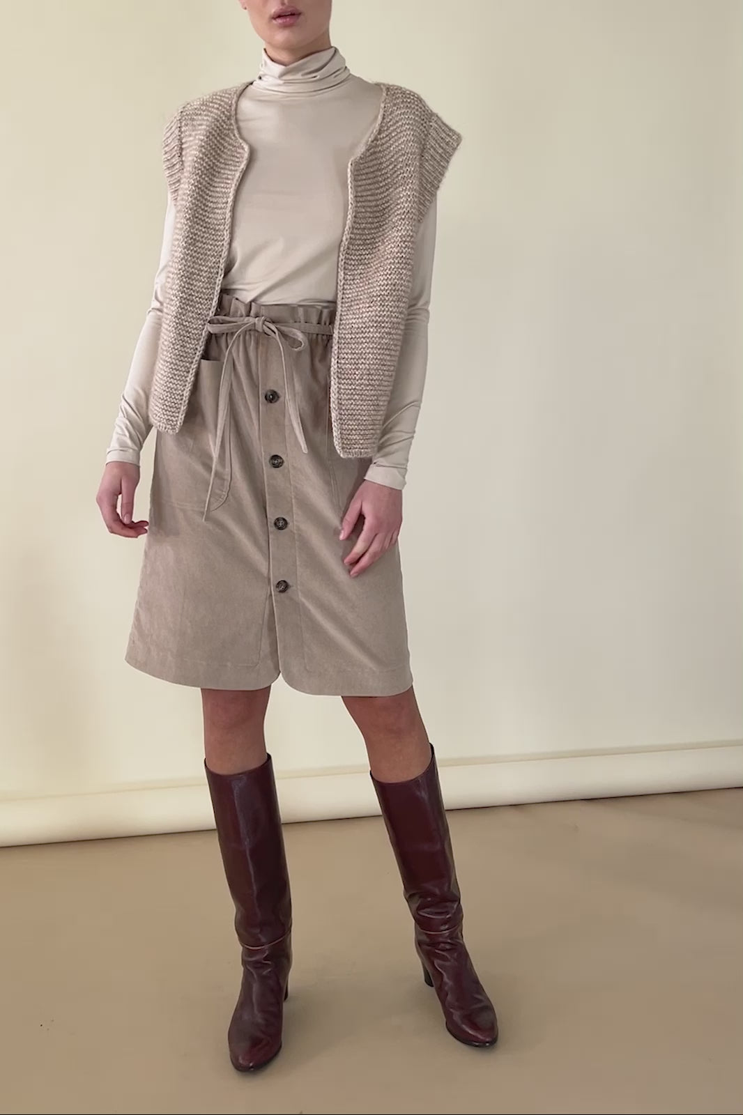 Woman in beige corduroy skirt, beige roll neck and knitted wool vest