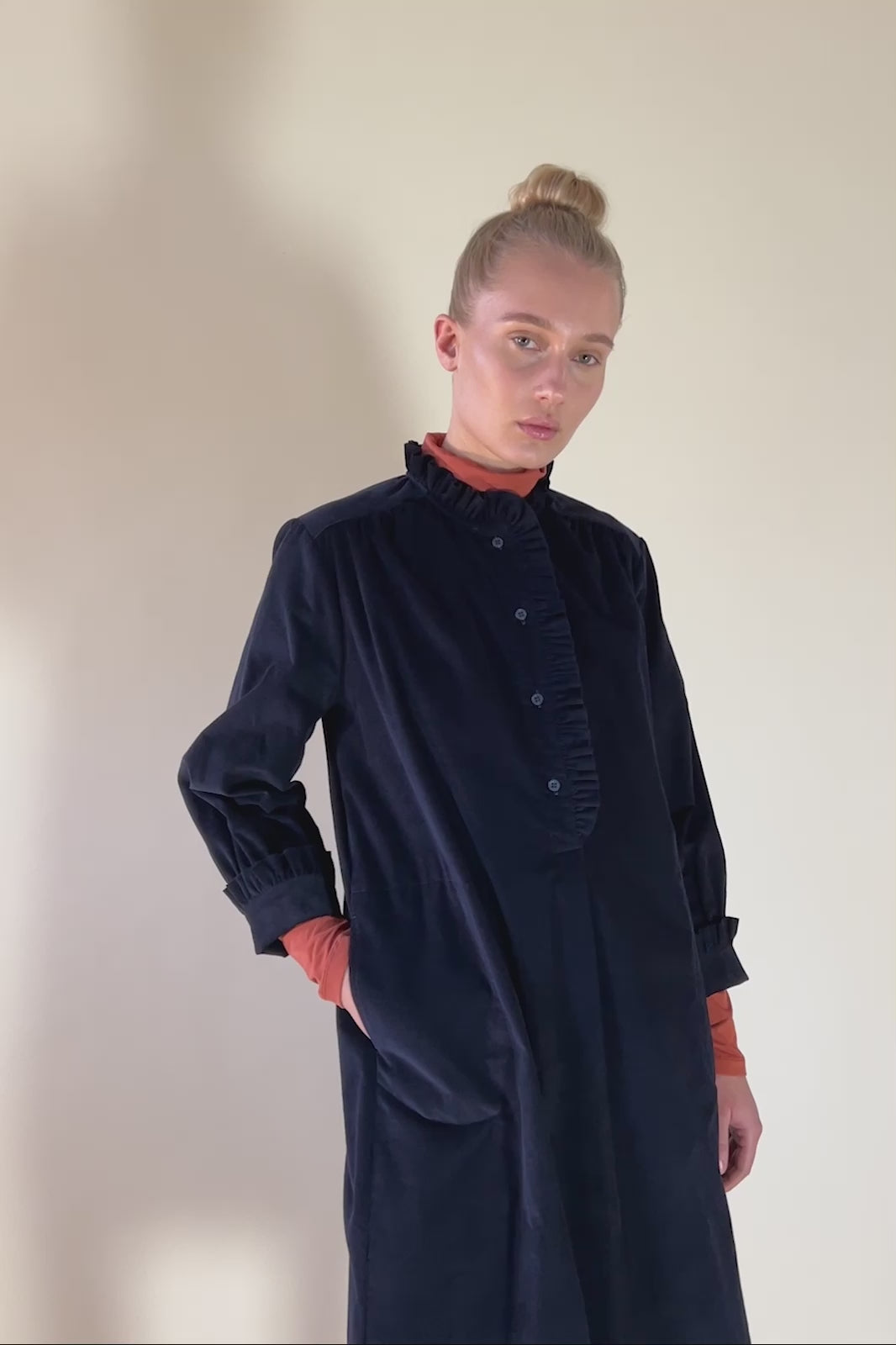 Woman in navy blue baby corduroy dress with buttons ad frill collar and orange roll neck beneath