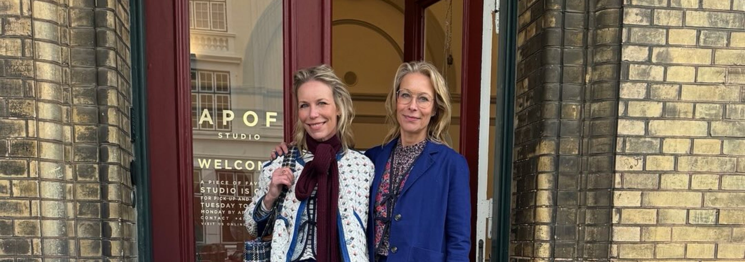 Kathrine and Frederikke Hviid standing outside APOF studio with a glass door and brick wall.