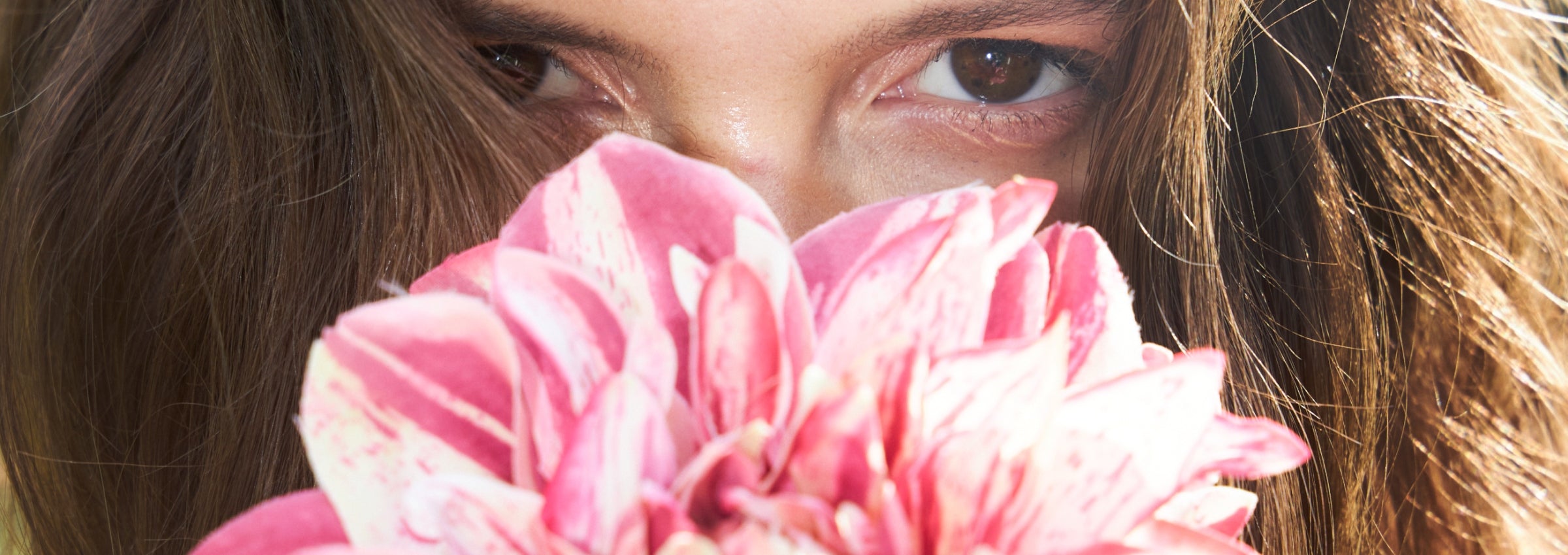 Close-up of a pink flower held by a person with long hair.