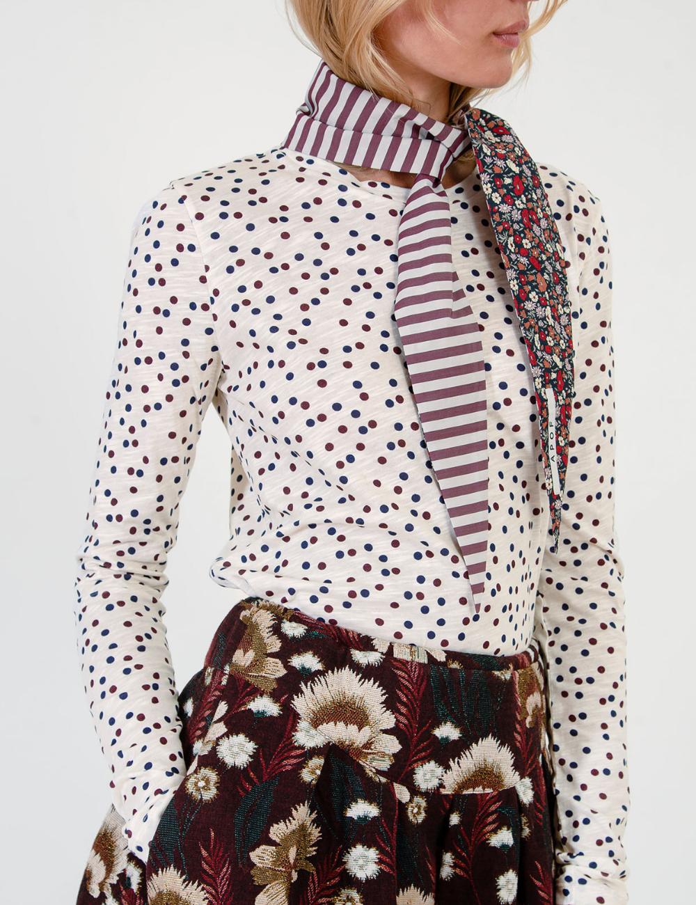 Woman in dot patterend long sleeve t-shirt, striped and floral patterned scarf and brown floral skirt