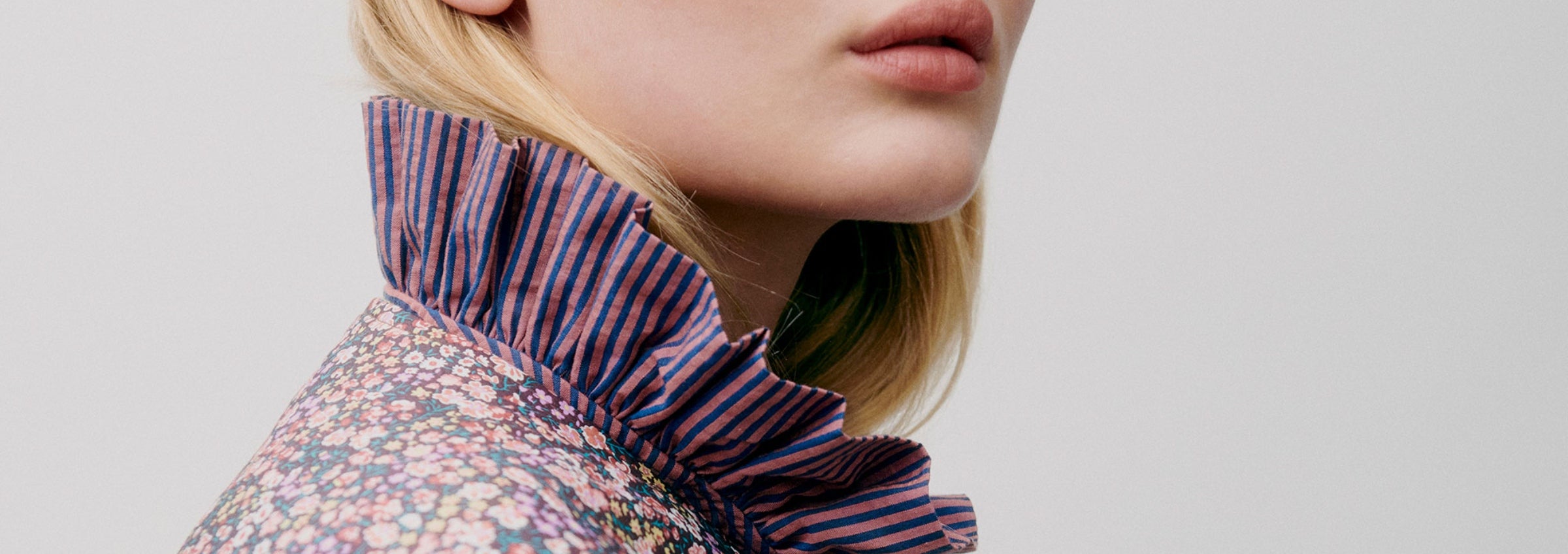 Close-up of a woman wearing a floral blouse with a ruffled collar against a light background