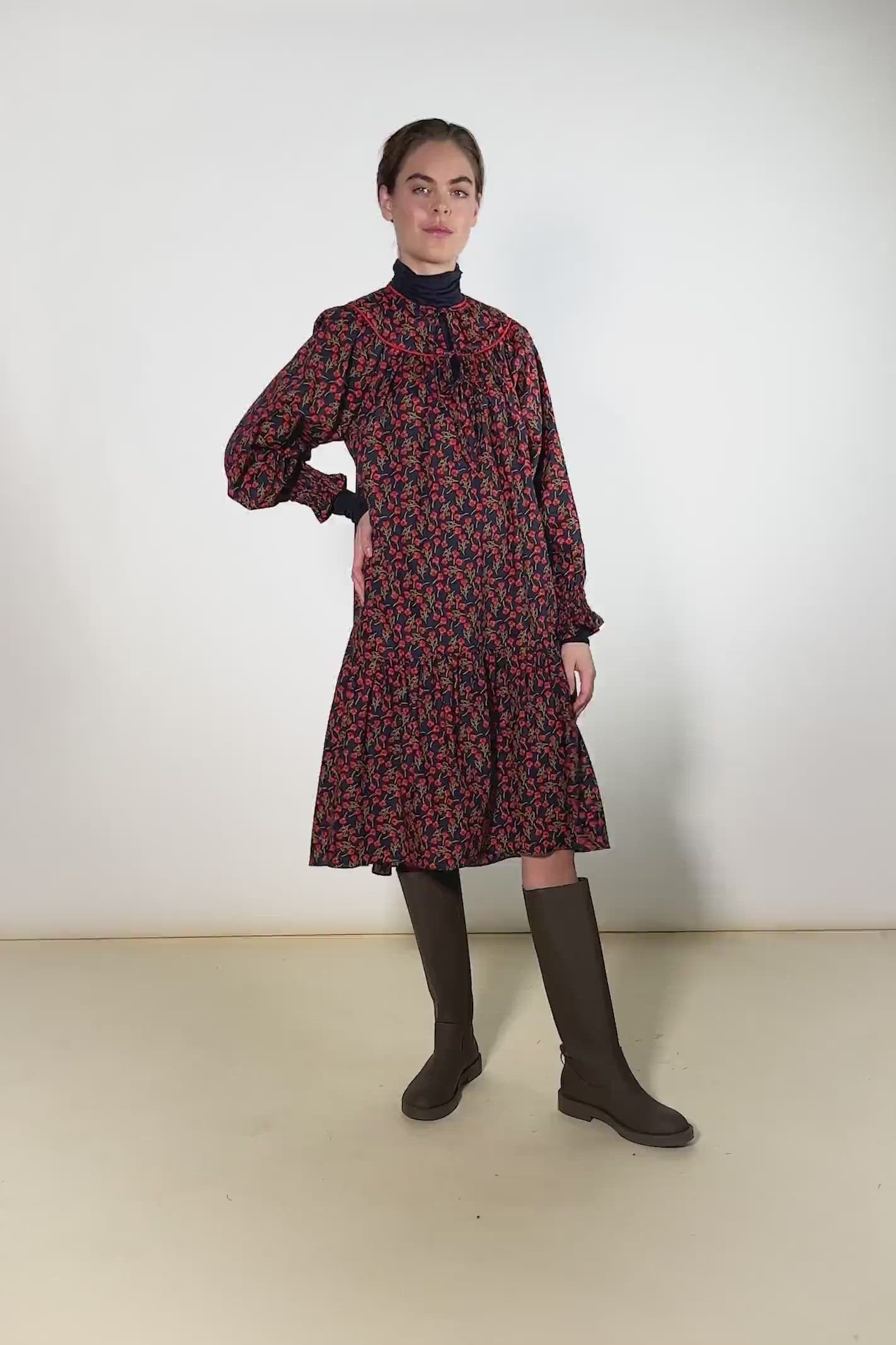 Woman in short Liberty cotton dress with red rose pattern and puffed sleeves with detailed cuffs