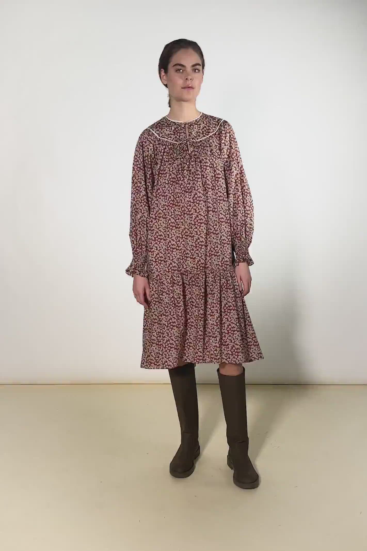 Woman in cotton dress with brown and red flower pattern and puffed sleeves with detailed cuffs and black boots