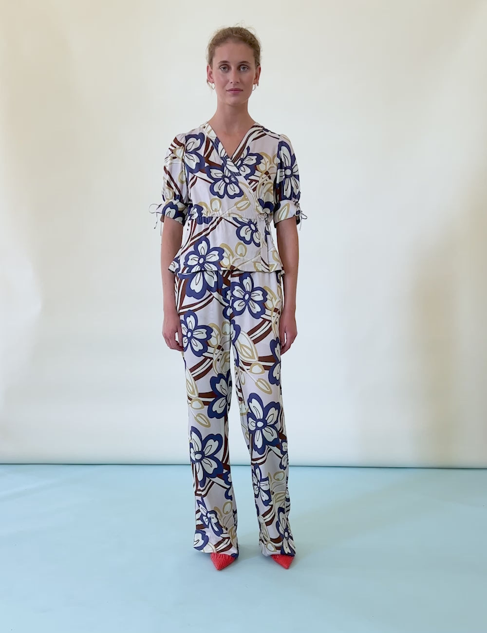 Woman in pants and short sleeved viscose wrap shirt with large flower print in blue brown and yellow