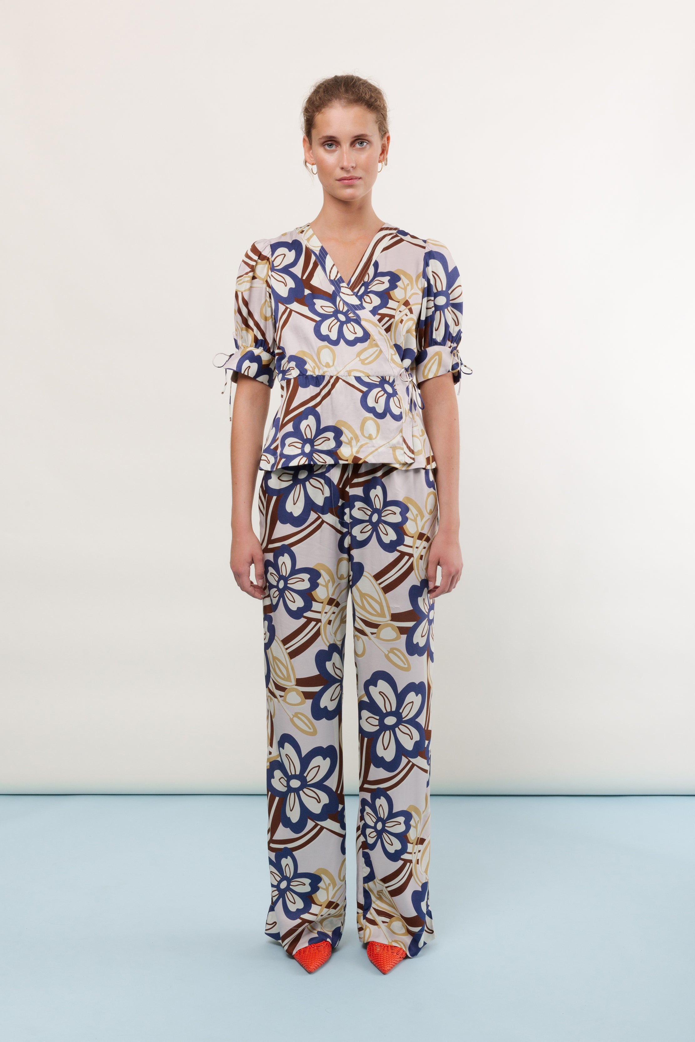 Woman in viscose pants and short sleeve blouse with large flower print in blue brown and yellow
