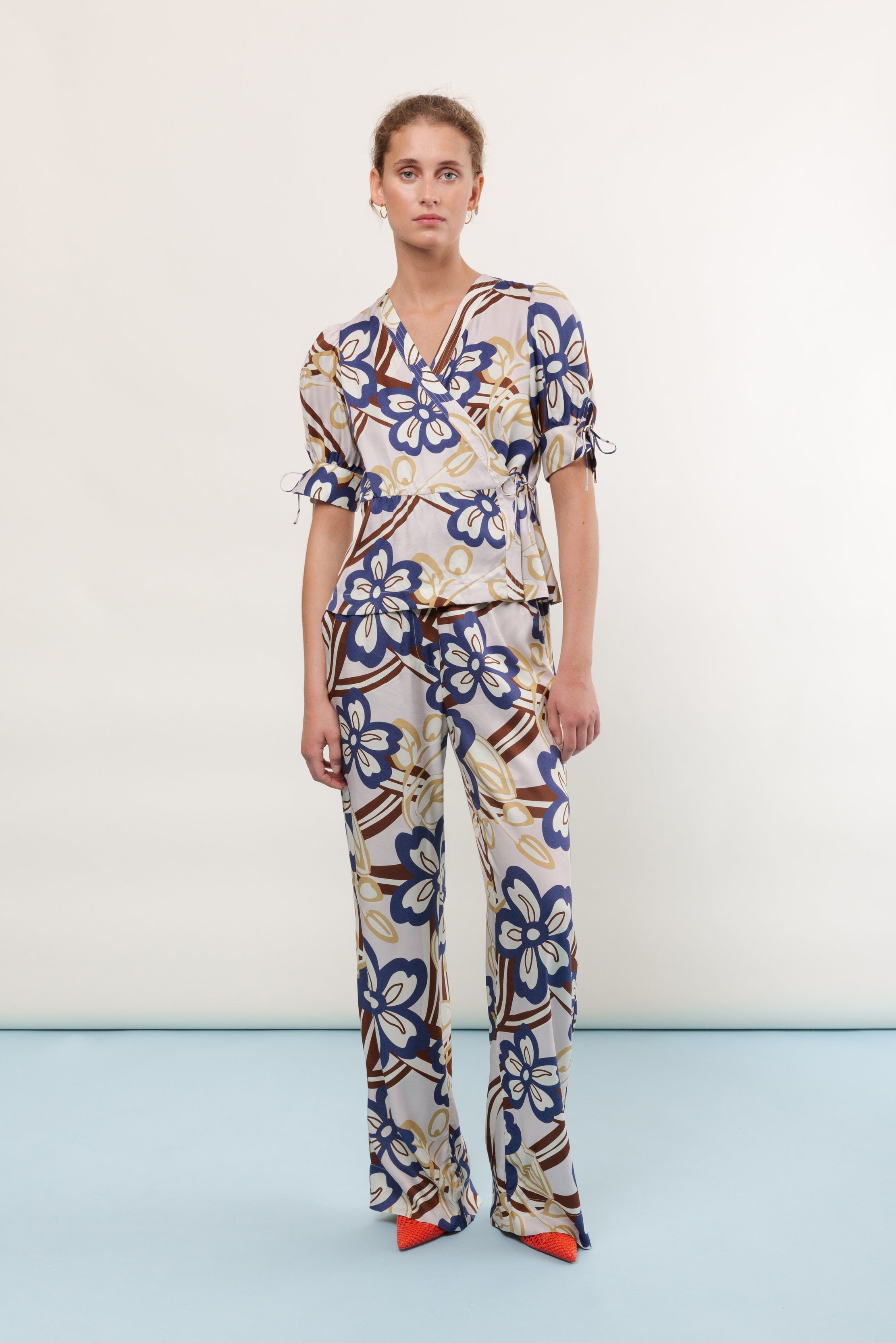 Woman in pants and short sleeved viscose wrap shirt with large flower print in blue brown and yellow