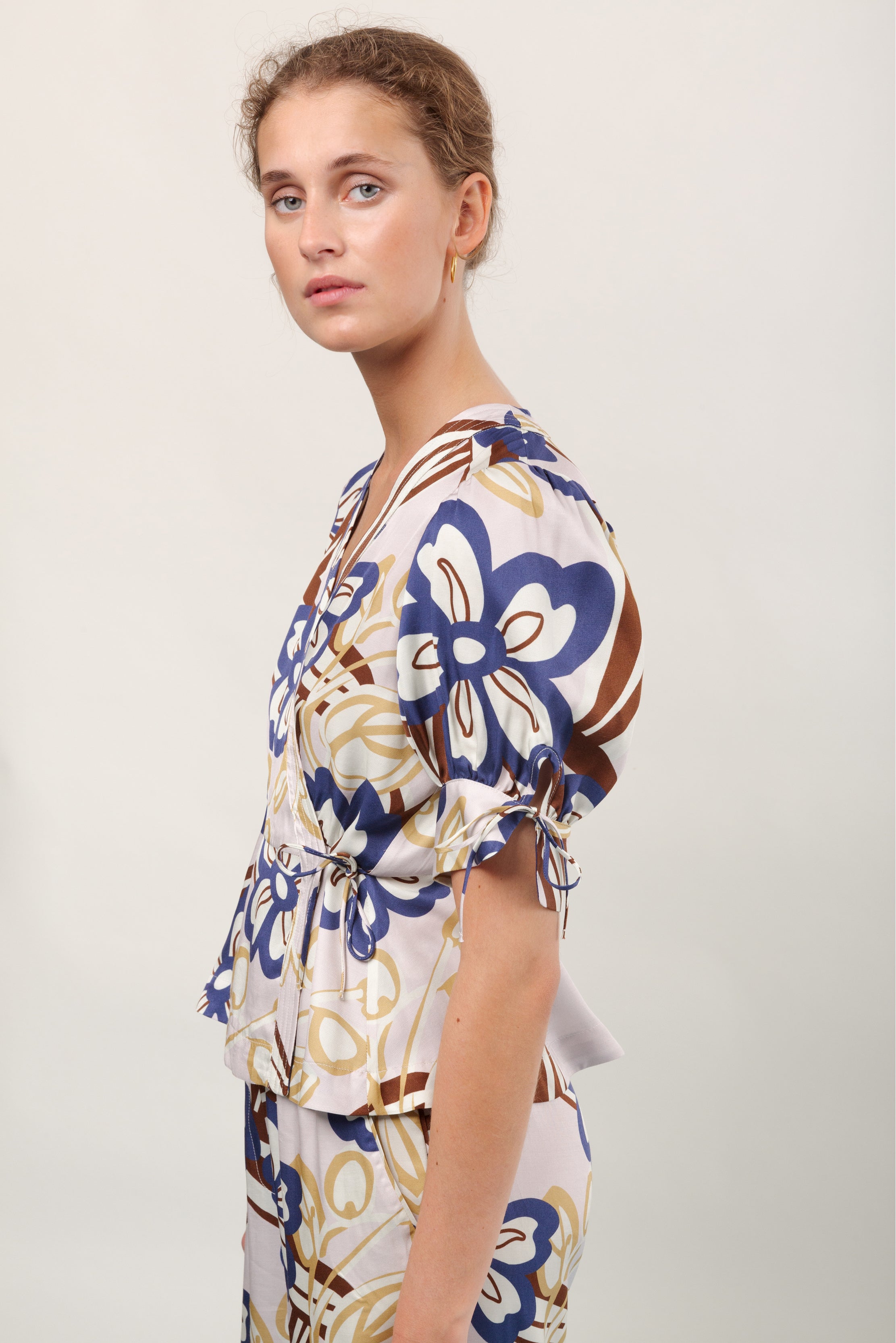 Woman in pants and short sleeved viscose wrap shirt with large flower print in blue brown and yellow