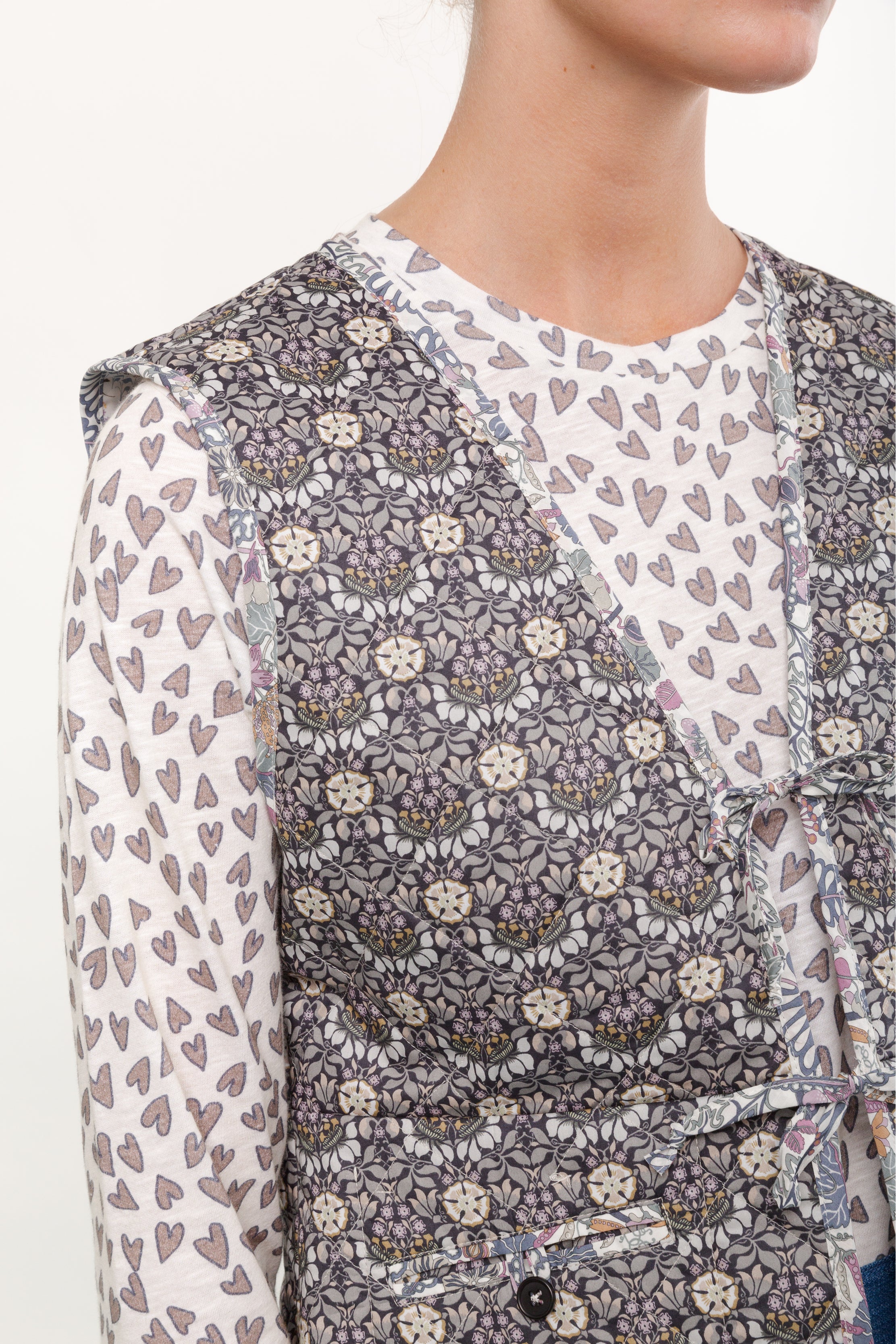 Kvinna i långärmad vit t-shirt med hjärtmönster och blommig väst