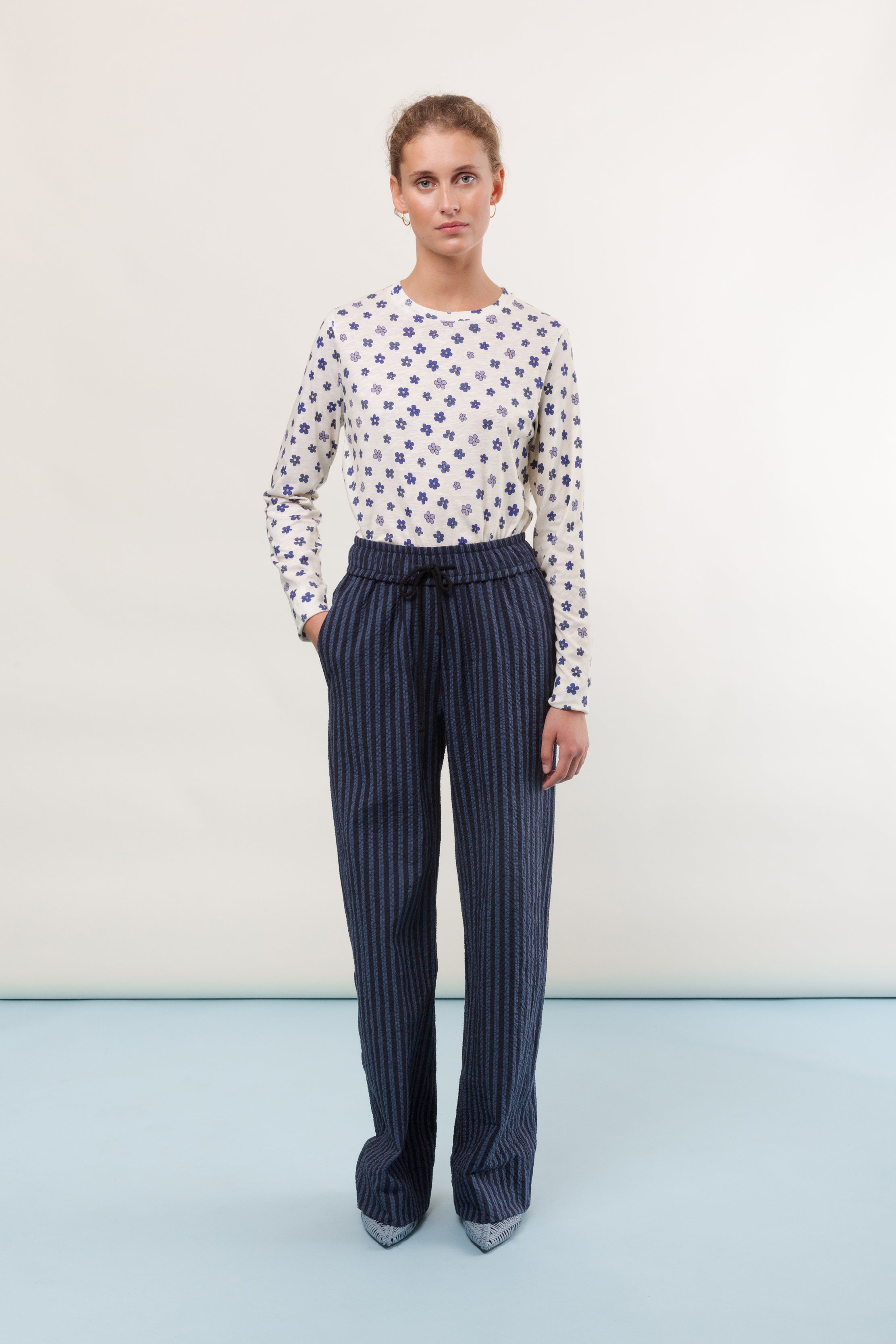 Woman in long sleeve white t-shirt with blue flower pattern and striped trousers