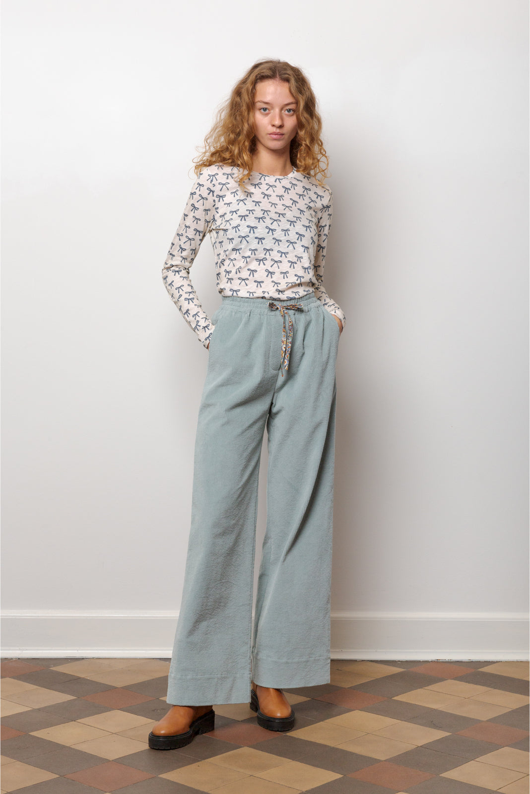 Kvinna i långärmad vit t-shirt med blå rosettmönster och blå byxor