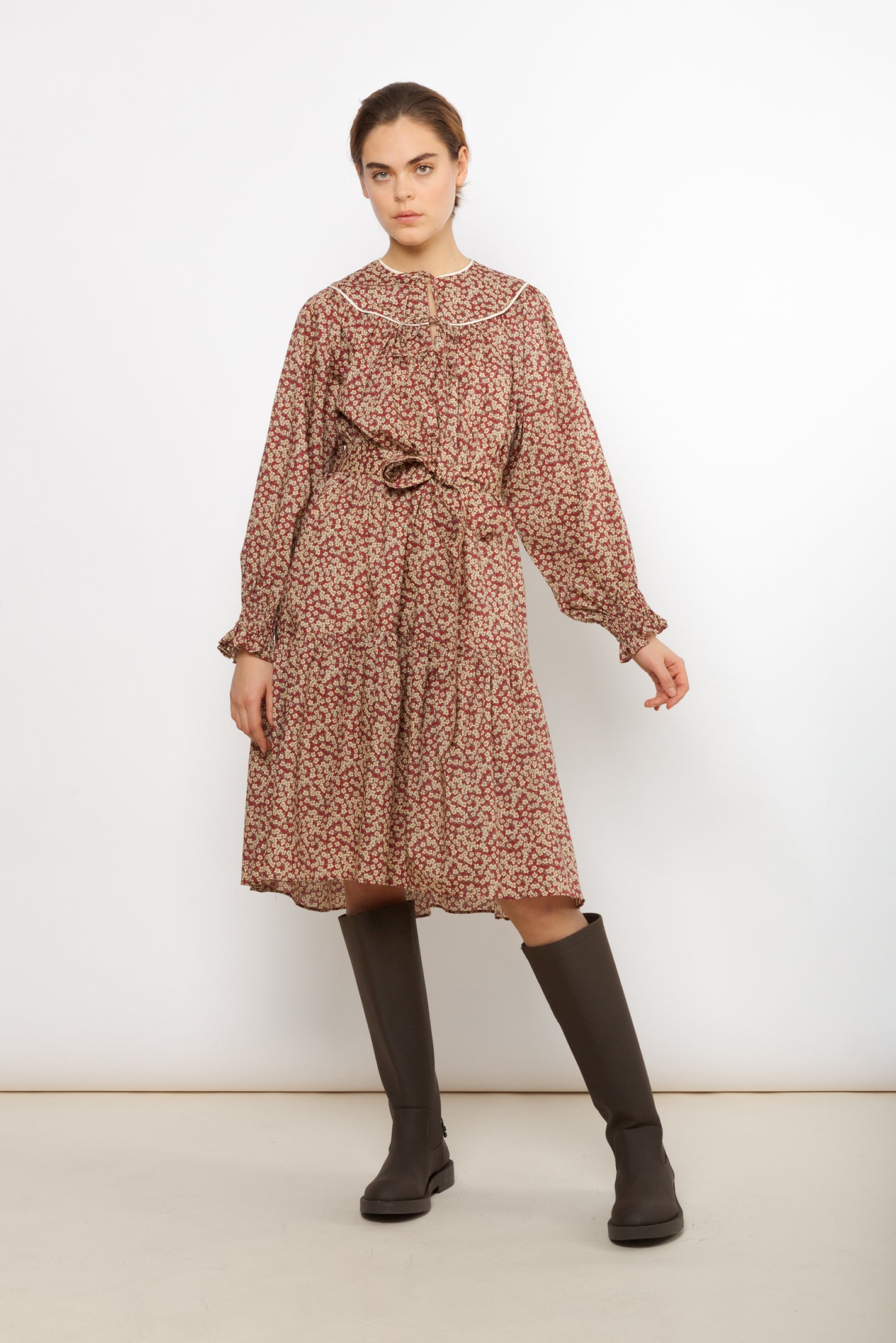 Woman in cotton dress with brown and red flower pattern and puffed sleeves with detailed cuffs and belt and black boots