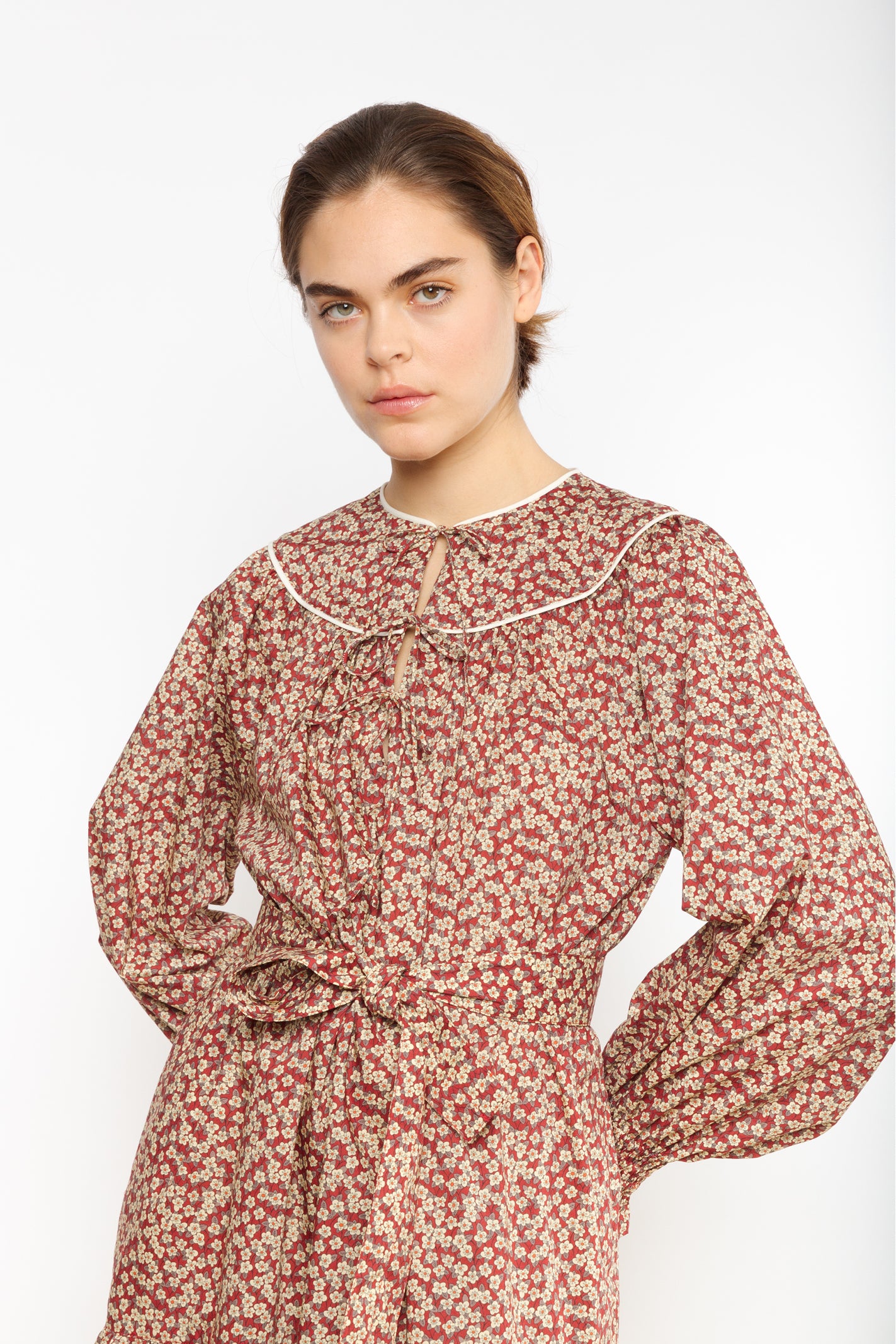 Woman in cotton dress with brown and red flower pattern and puffed sleeves with detailed cuffs and belt
