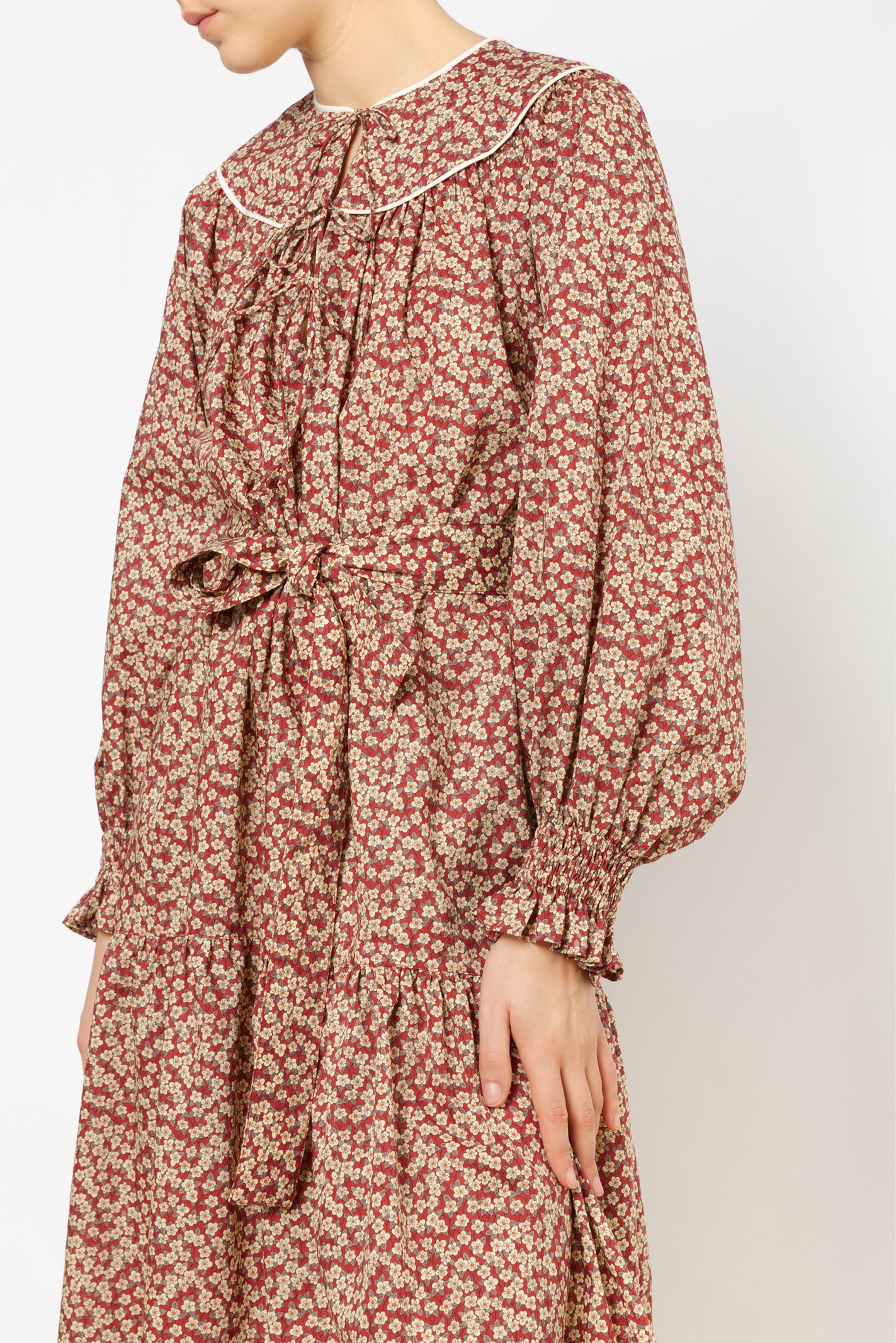Woman in cotton dress with brown and red flower pattern and puffed sleeves with detailed cuffs and black boots