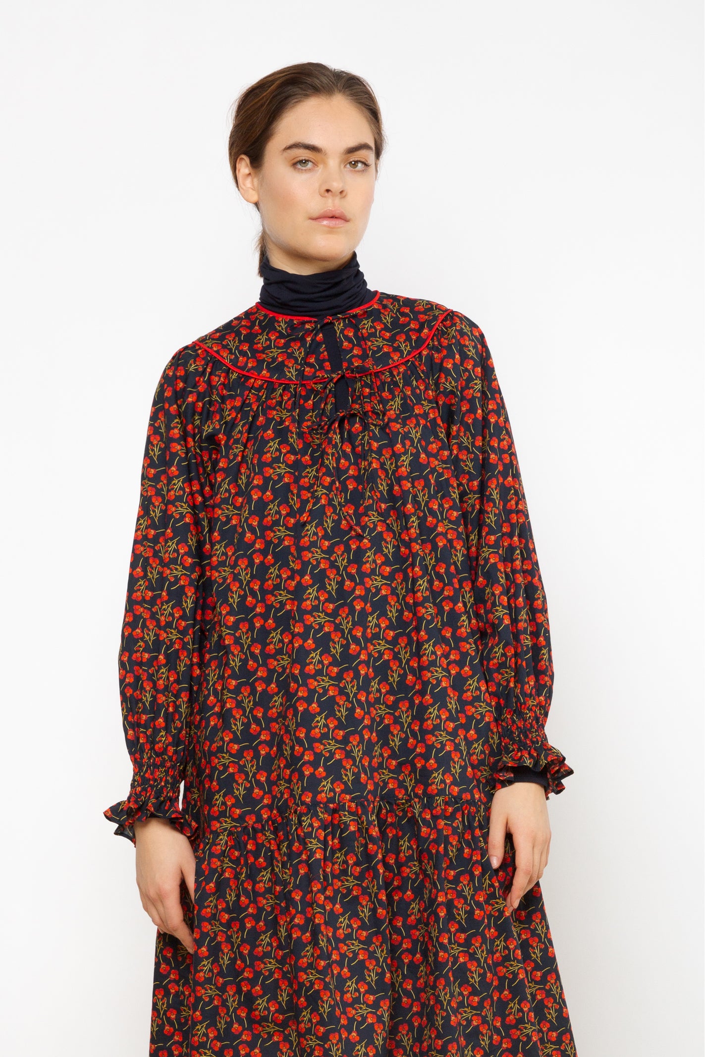 Woman in short Liberty cotton dress with red rose pattern and puffed sleeves with detailed cuffs