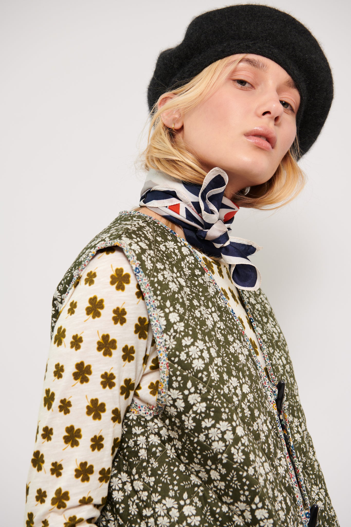 Woman in long sleeve white t-shirt with green four-leaved clovers pattern and green flower vest