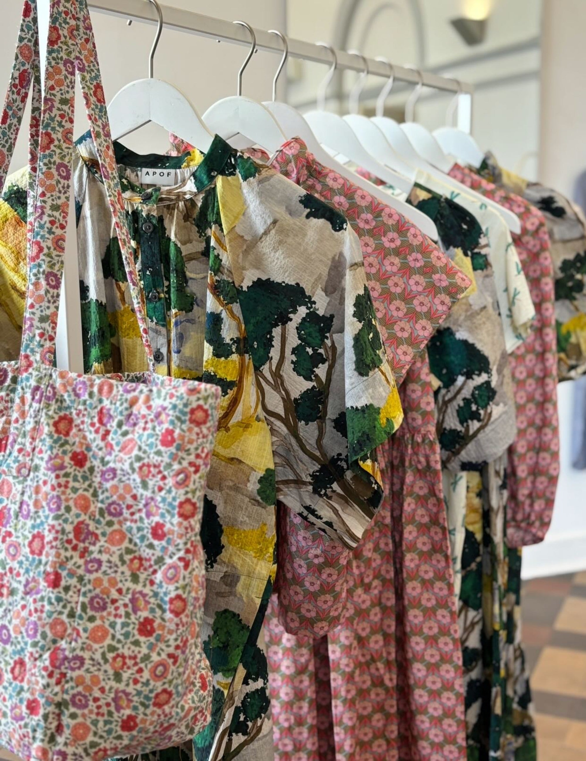 Rack with floral dresses, skirts and shirts and an APOF bag