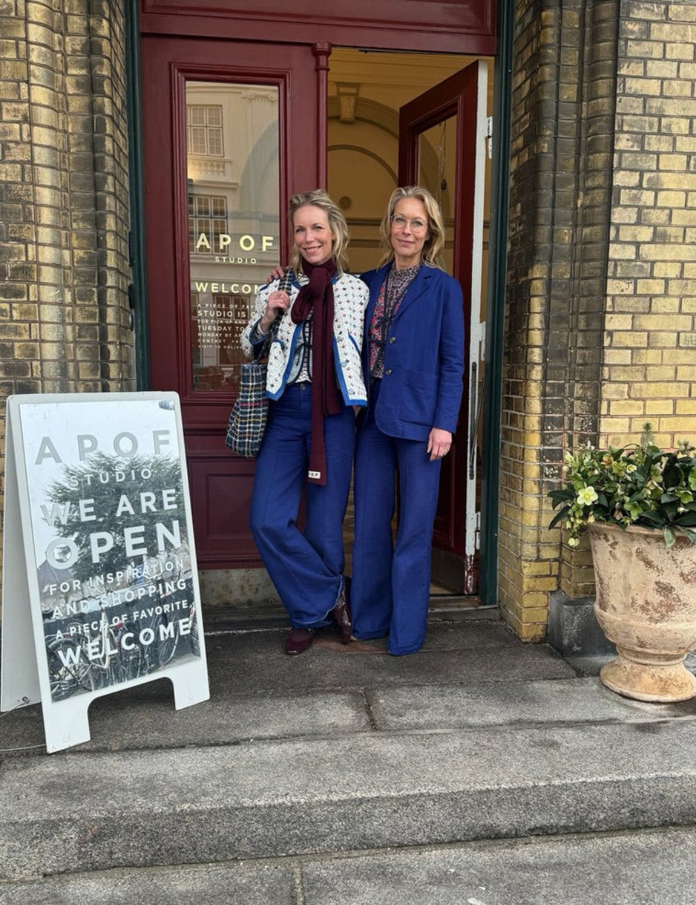 Kathrine and Frederikke Hviid standing outside APOF studio with a glass door and brick wall.