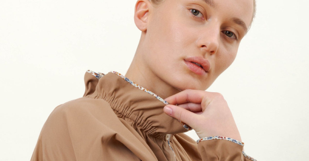 Woman in brown long sleeved shirt with ruffled stand collar and frilled cuffs with contrasting floral pipings