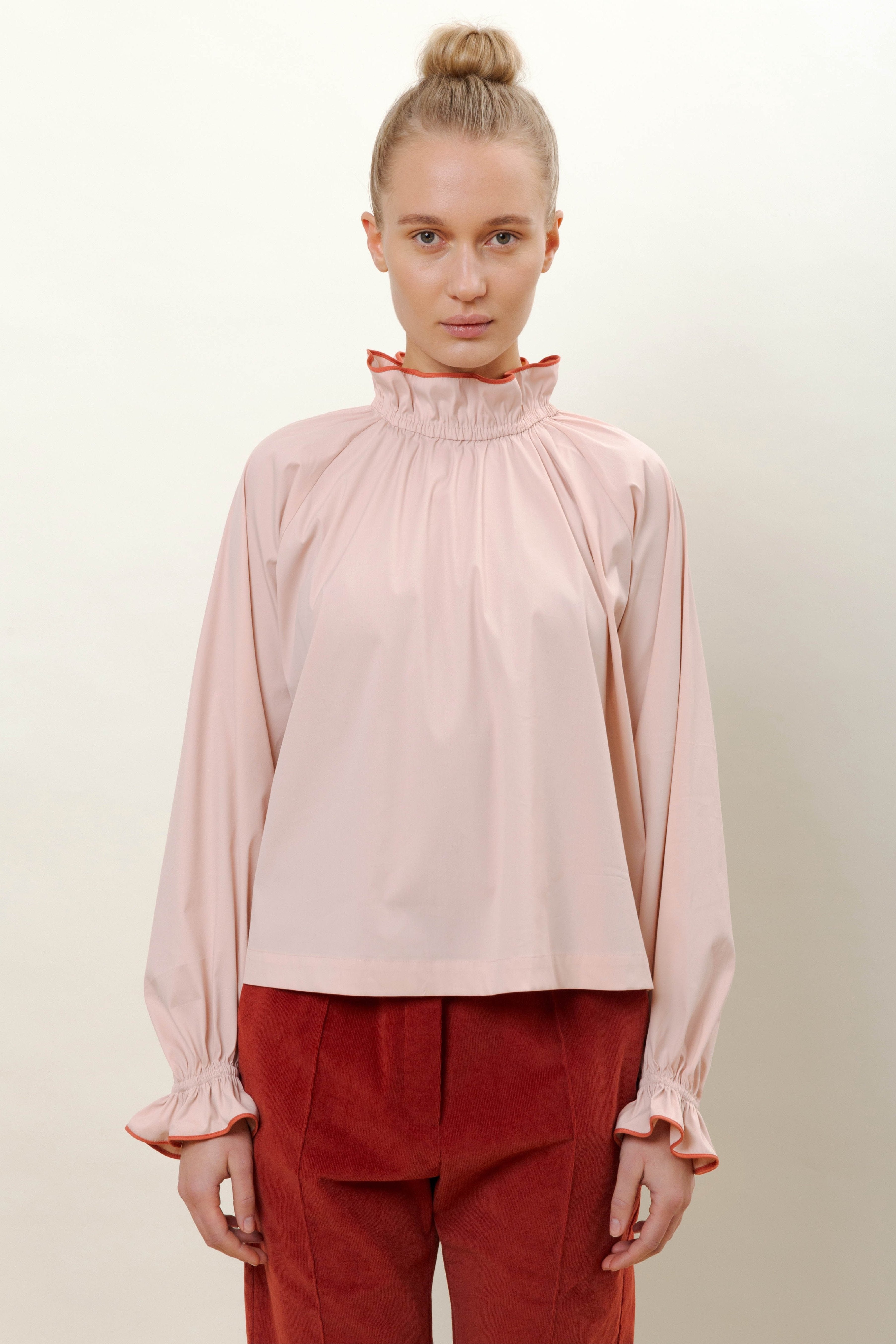 Woman in pink long sleeved shirt with ruffled collar and red trousers