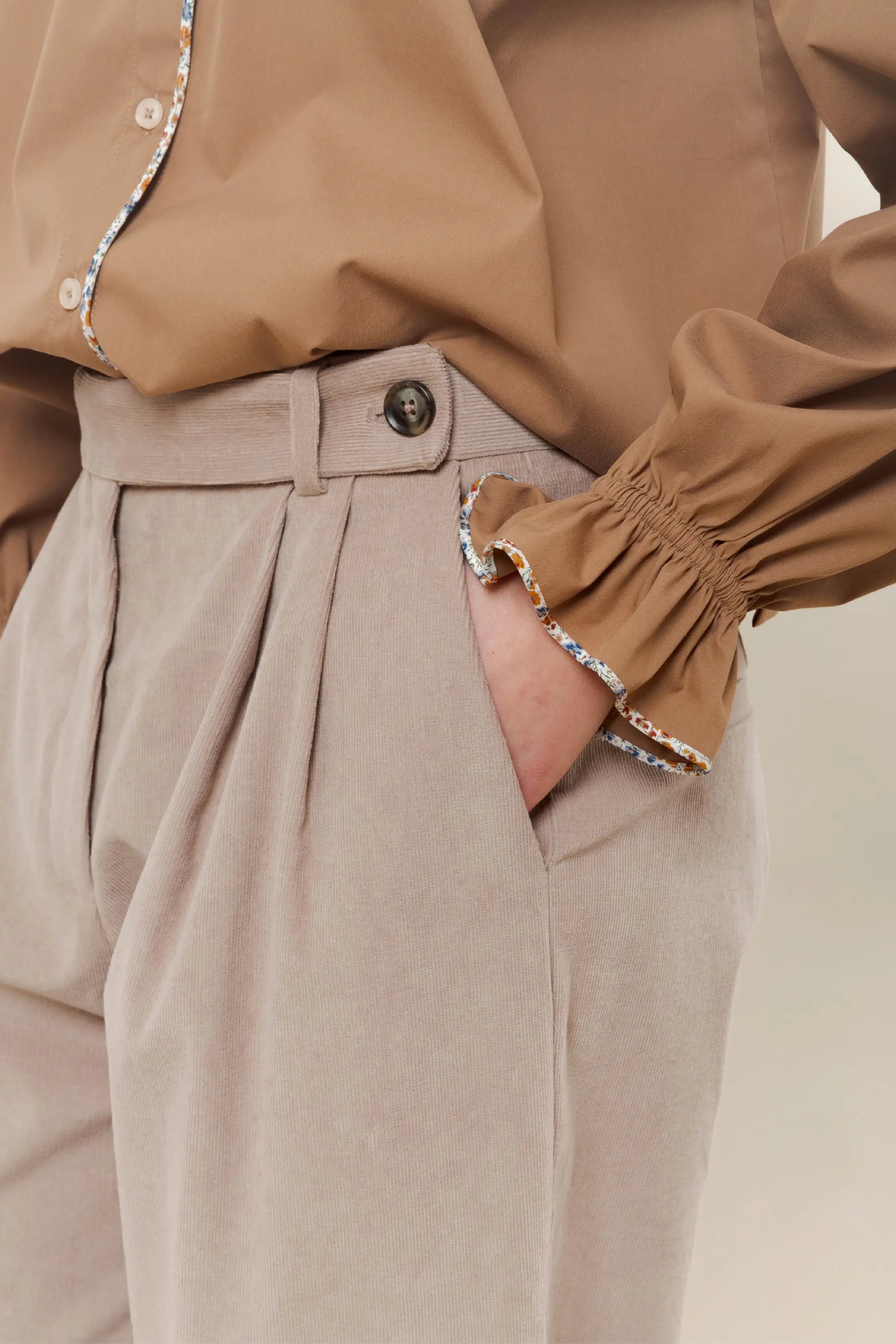 Woman in beige trousers and brown shirt with long sleeves and ruffles