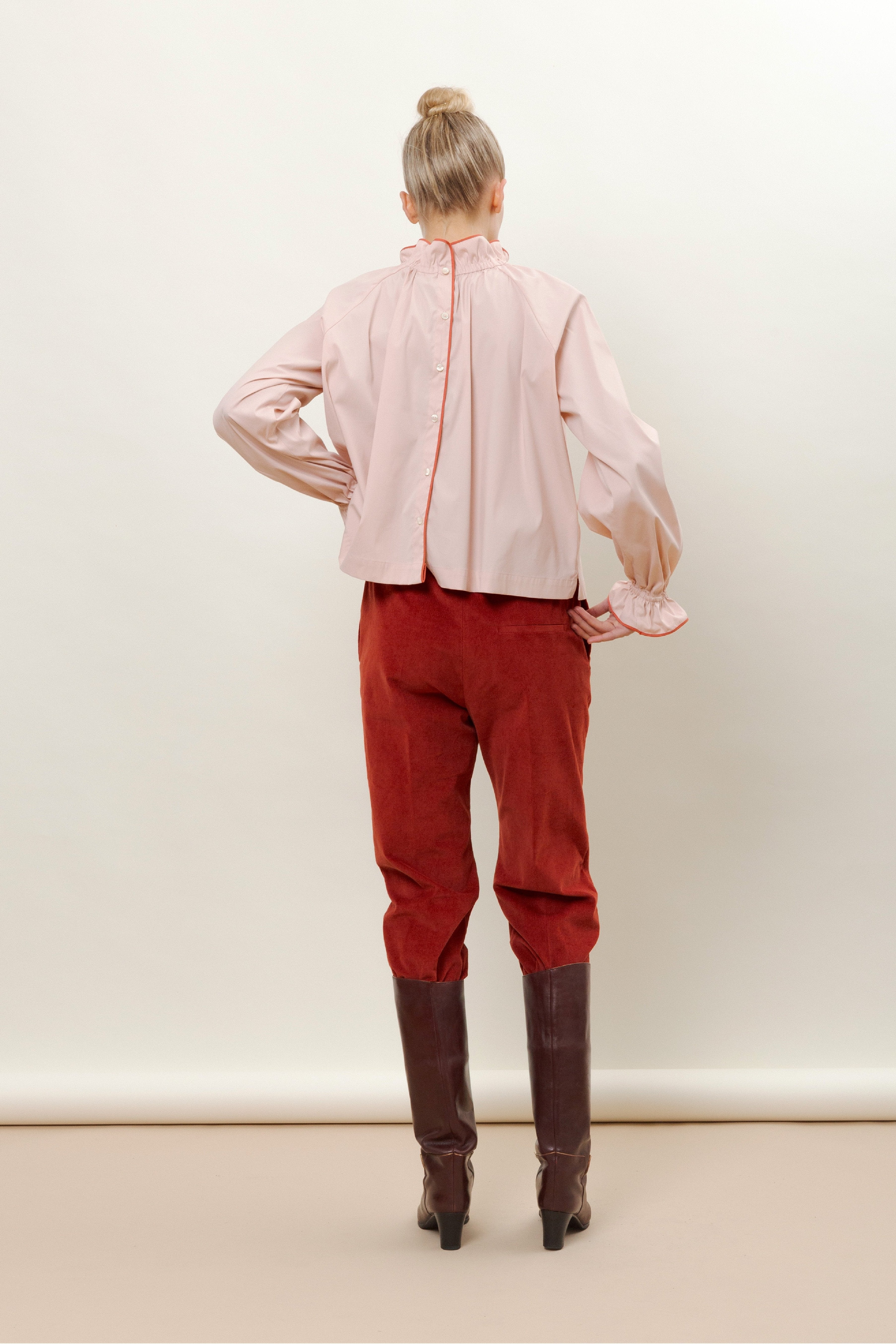 Woman in pink long sleeved shirt, red trousers and brown boots