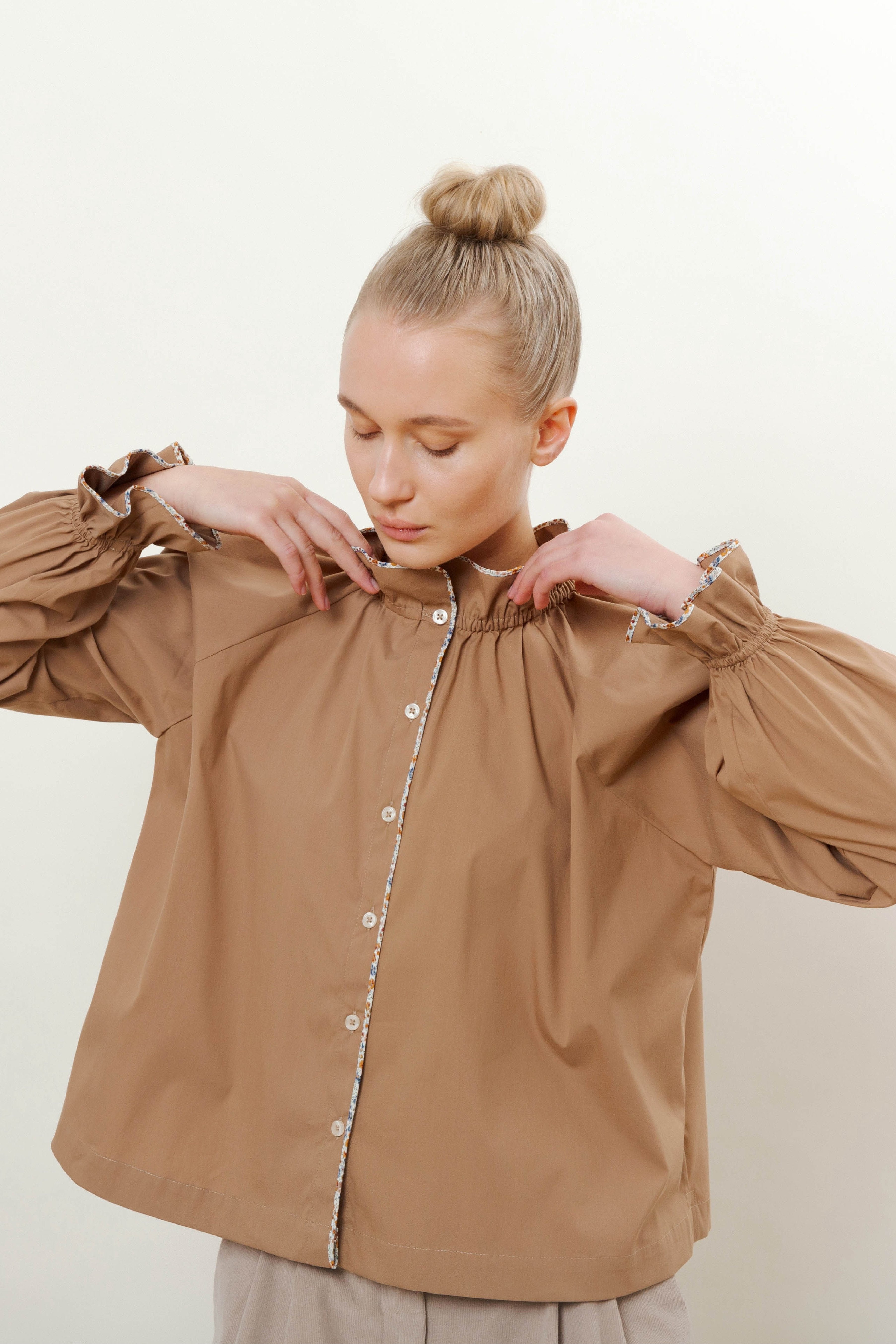 Woman in brown shirt with long sleeves, buttons, pipings and ruffles