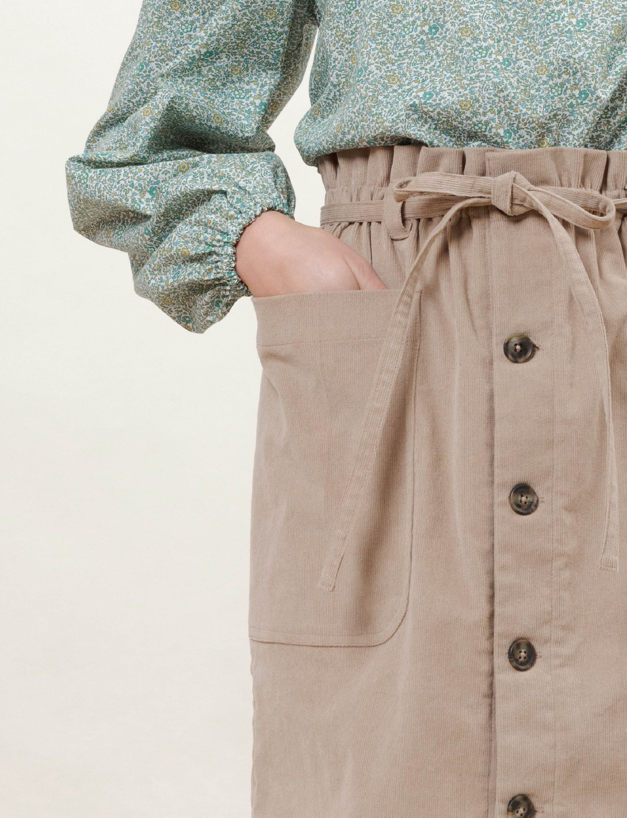 Woman in light pink skirt with buttons and pockets and green long sleeved blouse