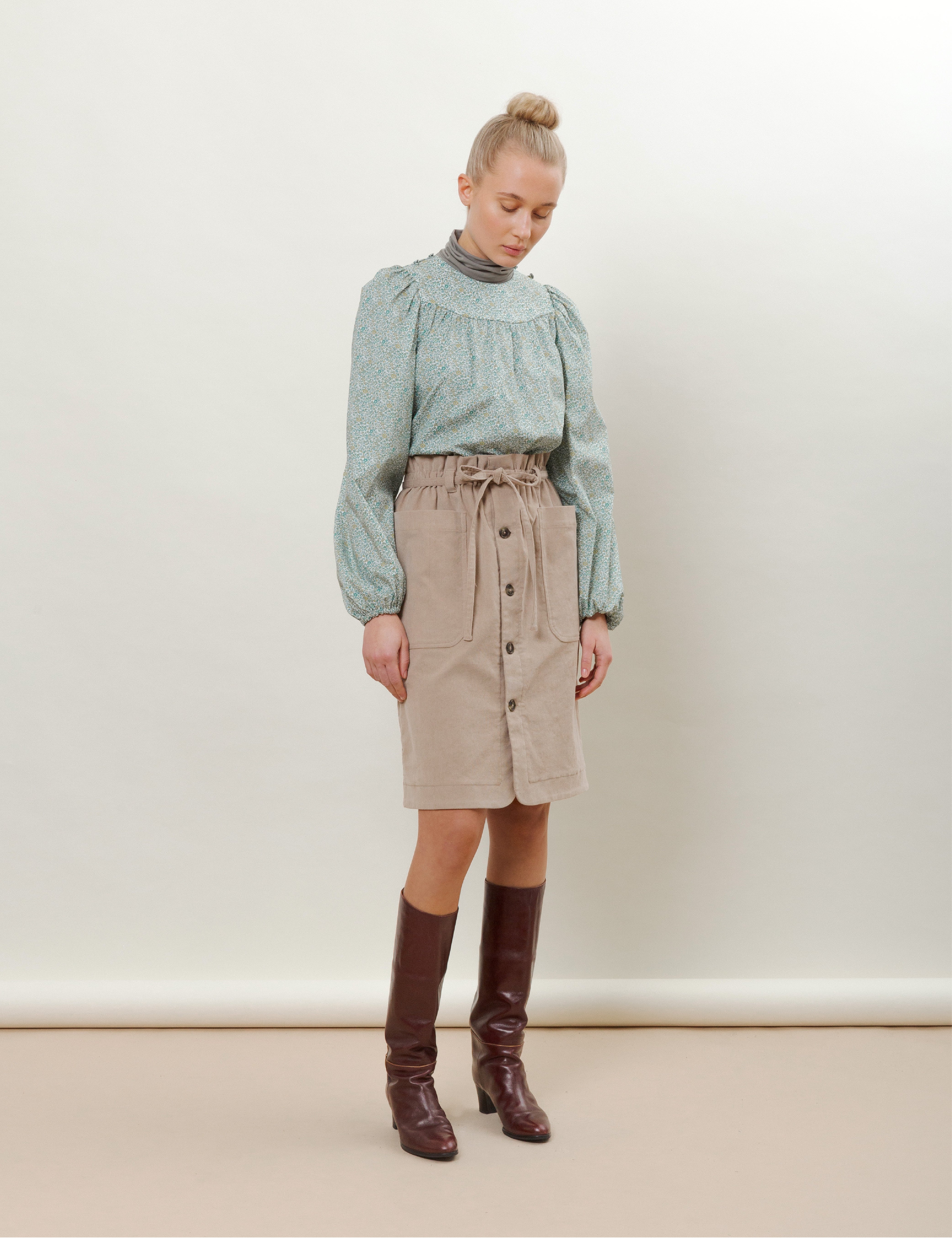 Woman in light pink skirt with buttons and pockets and green long sleeved blouse