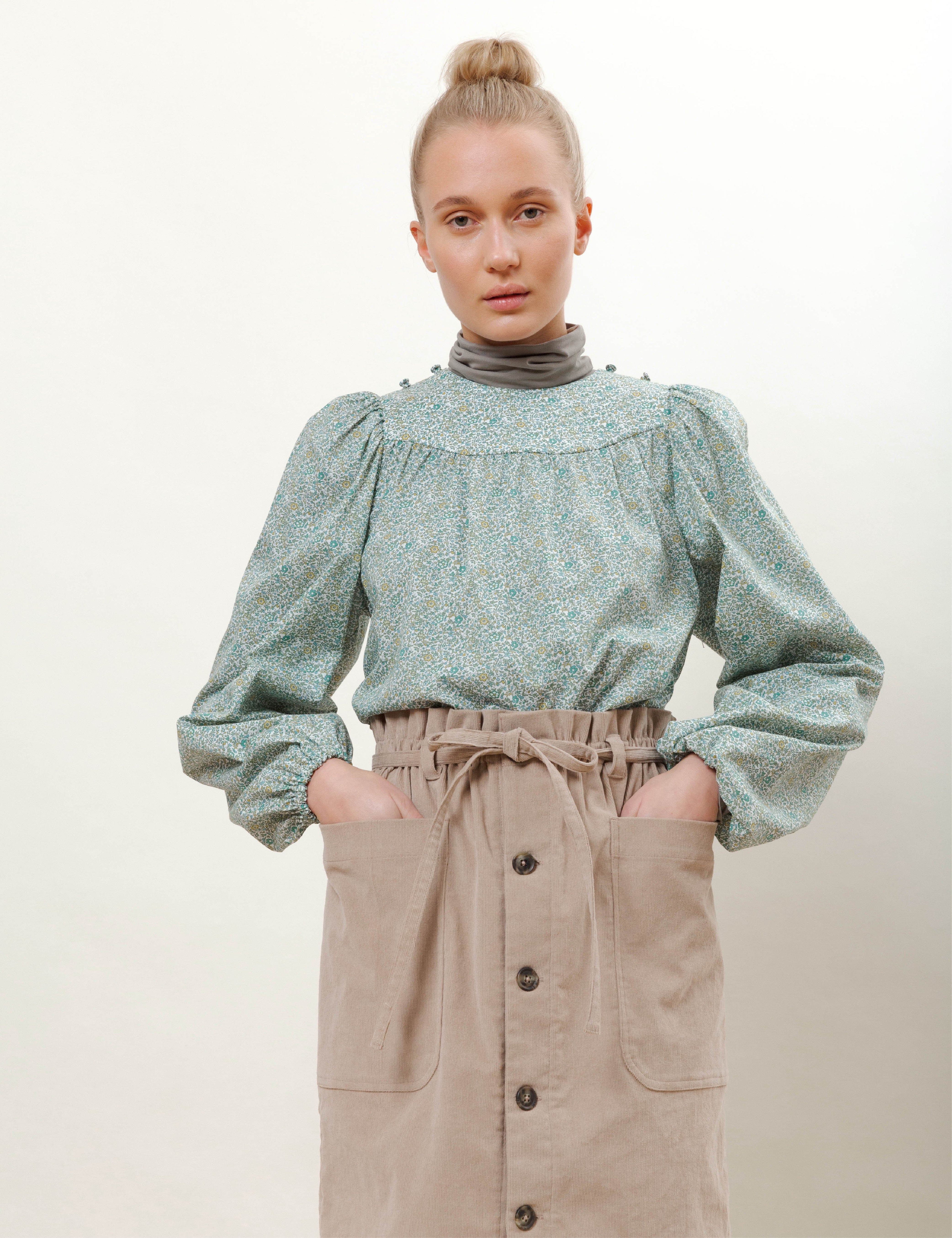 Woman in light pink skirt with buttons and pockets and green long sleeved blouse