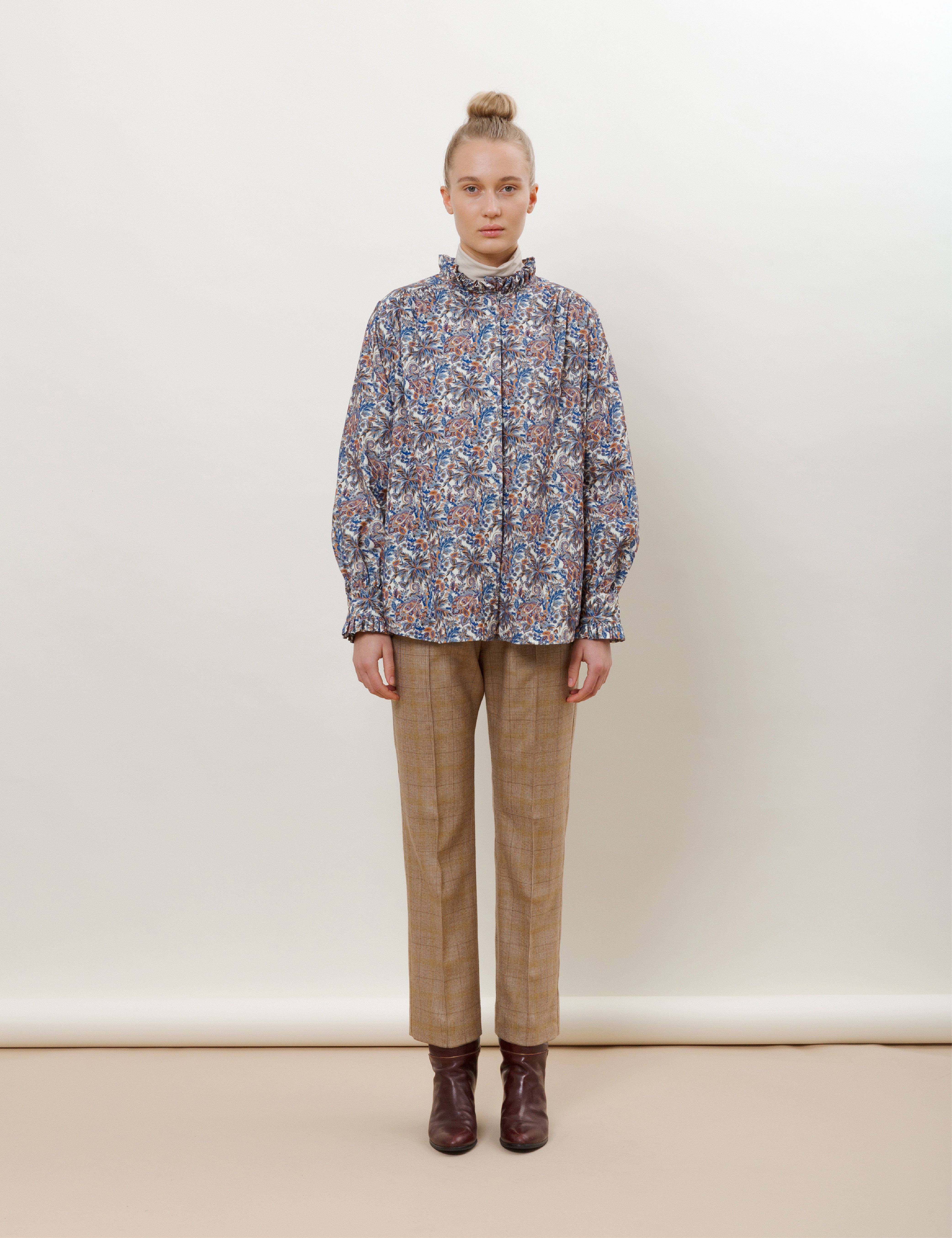 Woman in brown check wool pants, blue flower patterned blouse with frills and a beige roll-neck