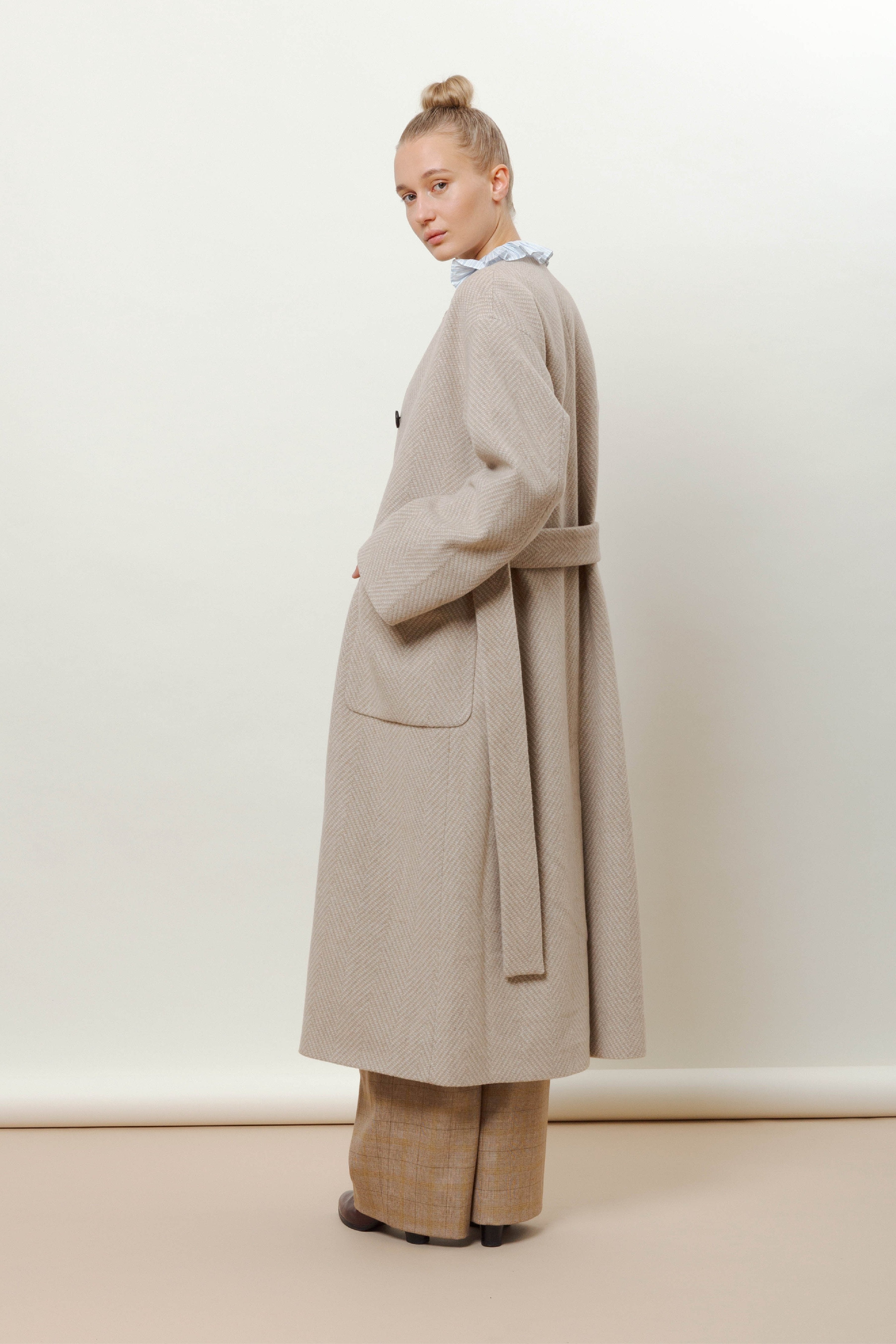 Woman in long beige wool coat with herringbone pattern, belt and pockets