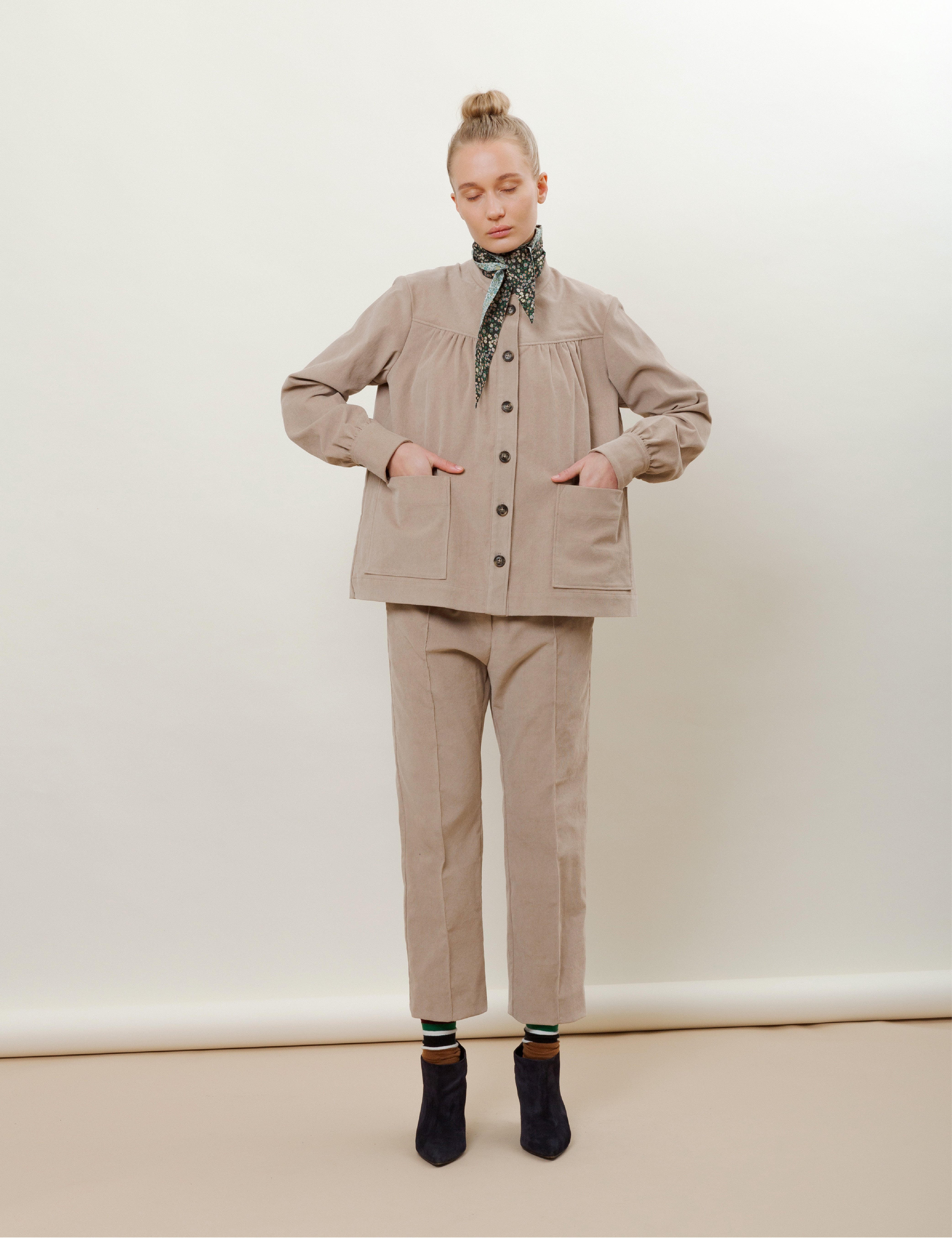 Woman in beige corduroy pants with cigarette silhouette and beige jacket with pockets and buttons