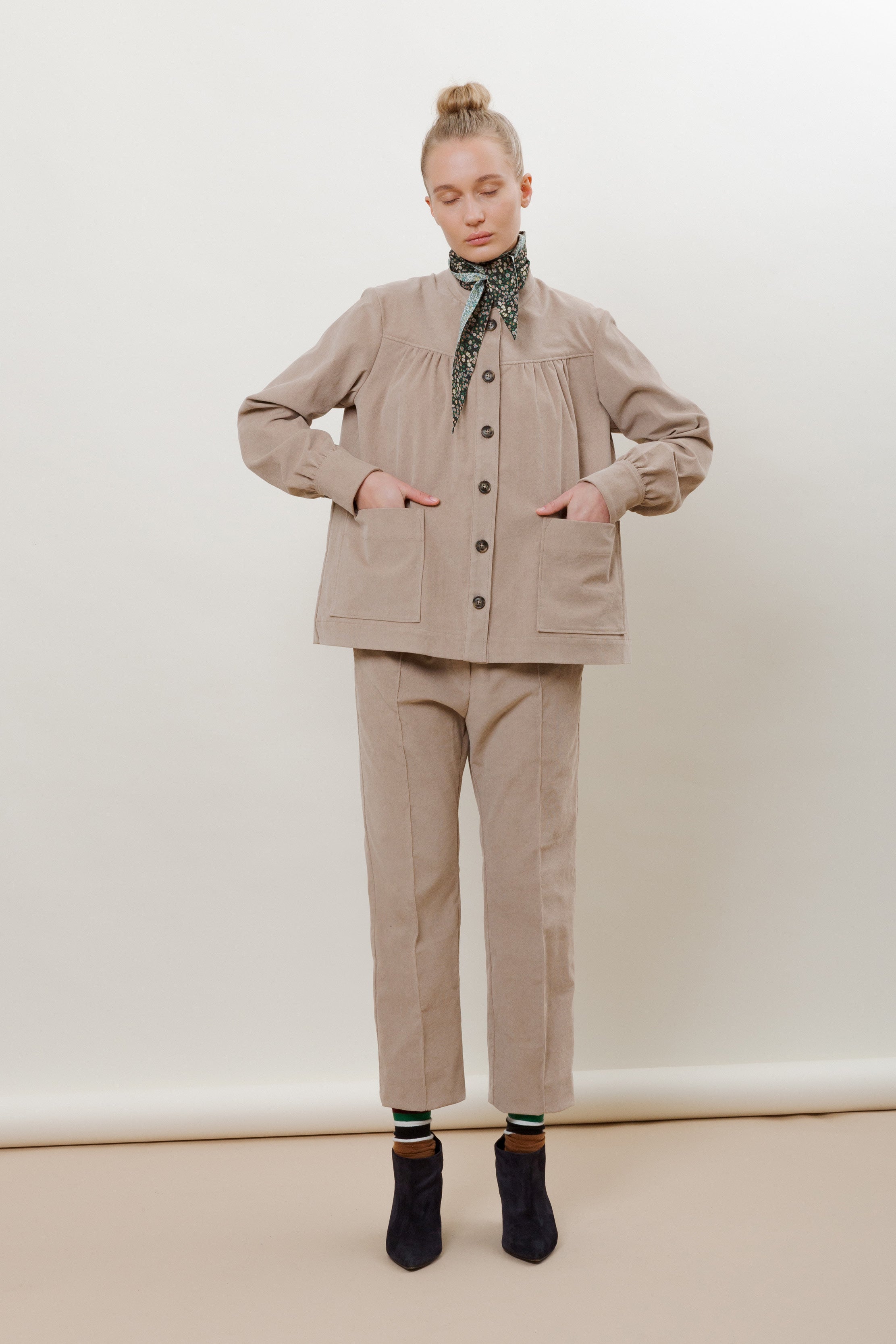 Woman in beige baby corduroy pants and jacket with buttons and floral print bandana around neck