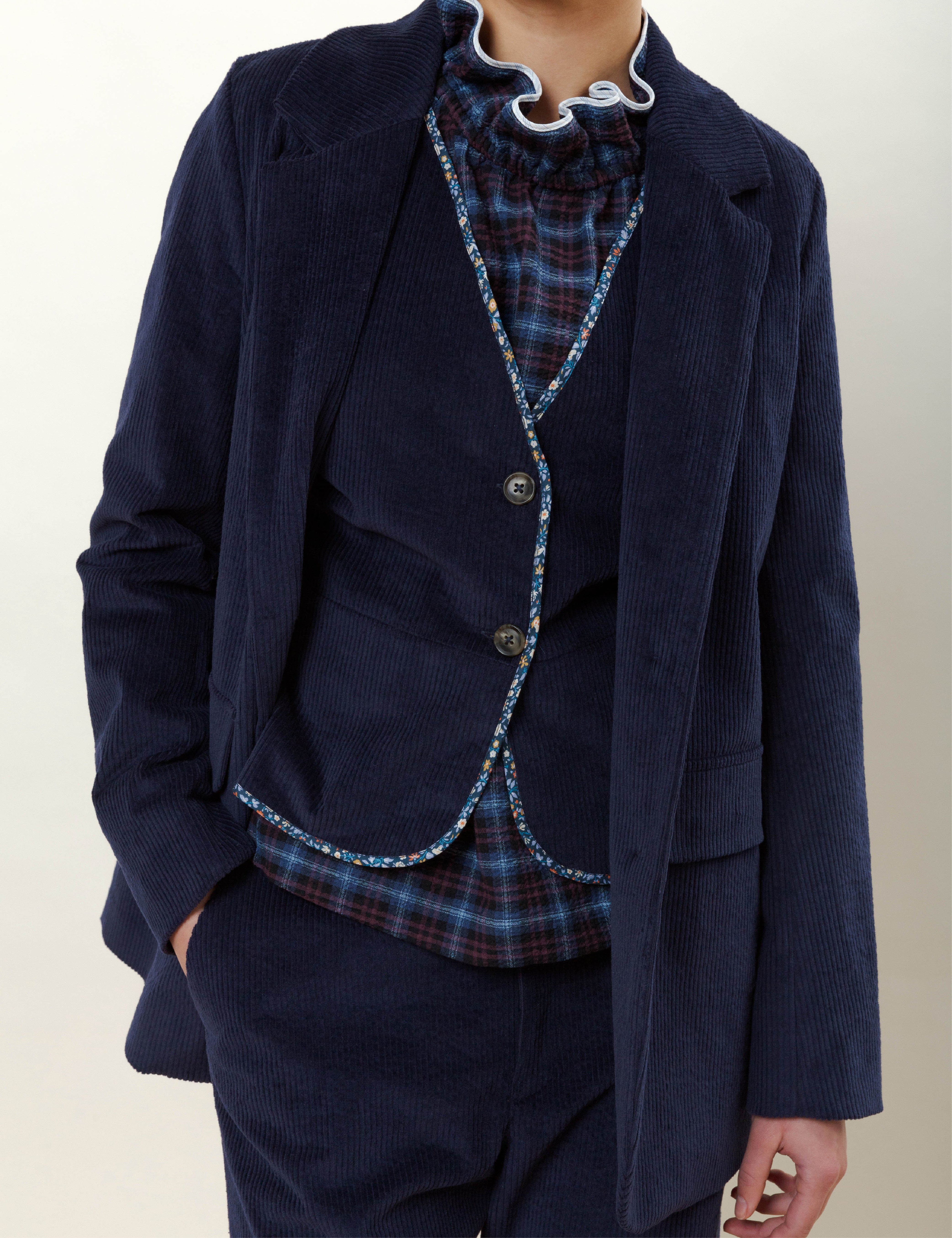 Woman in blue corduroy jacket and wide pants, vest and blue checked blouse with ruffles