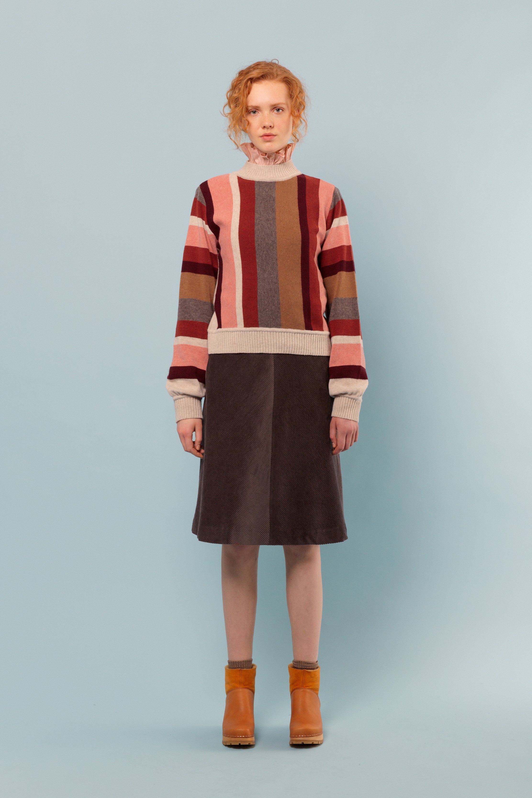 Woman in Striped wool pullover in pink, beige, brown and red, frilled pink blouse and brown skirt