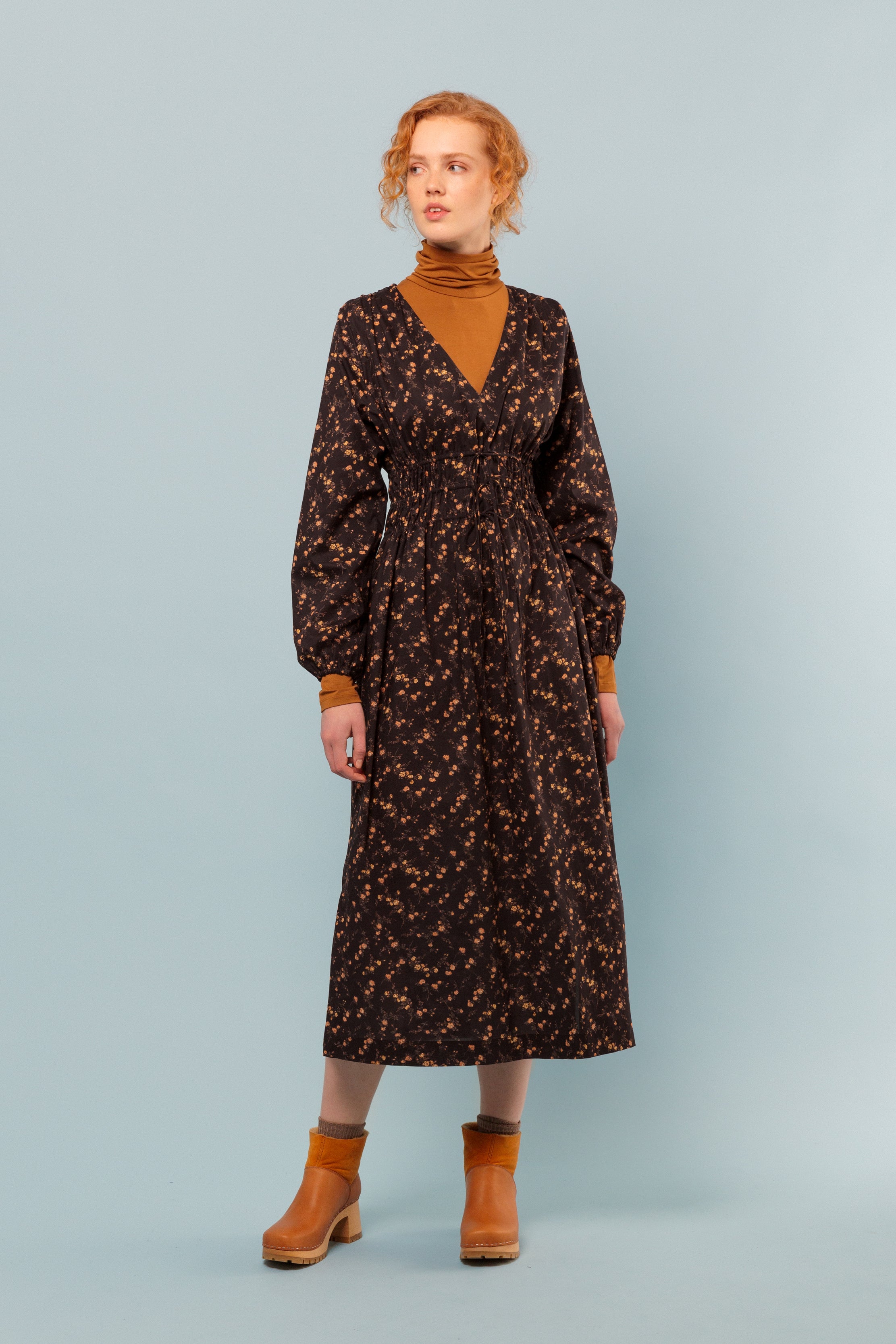 Woman in brown and orange long dress in Liberty flower print cotton with long sleeves and v-neck, orange roll neck and boots