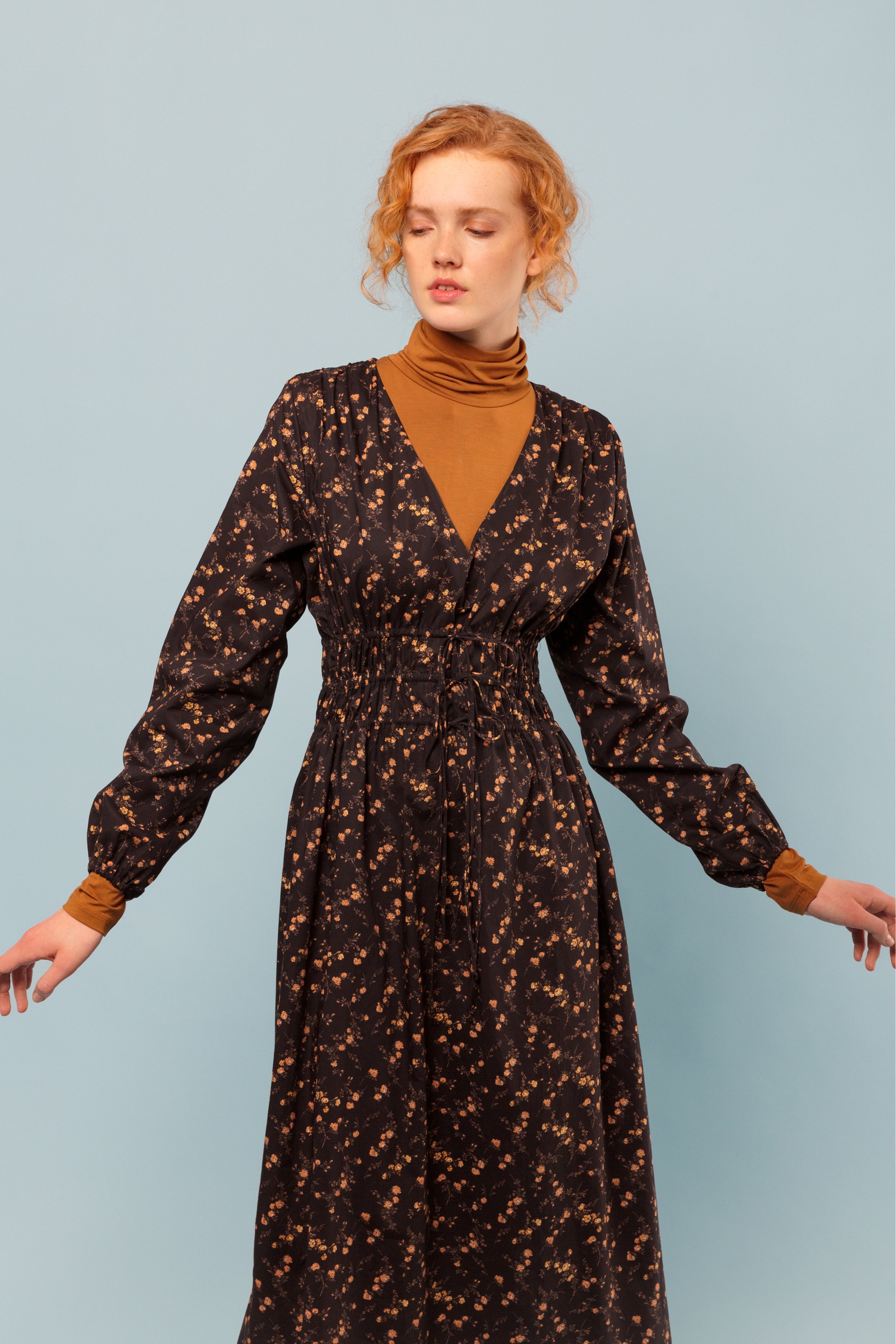 Woman in brown and orange long dress in Liberty flower print cotton with long sleeves and v-neck and orange roll neck